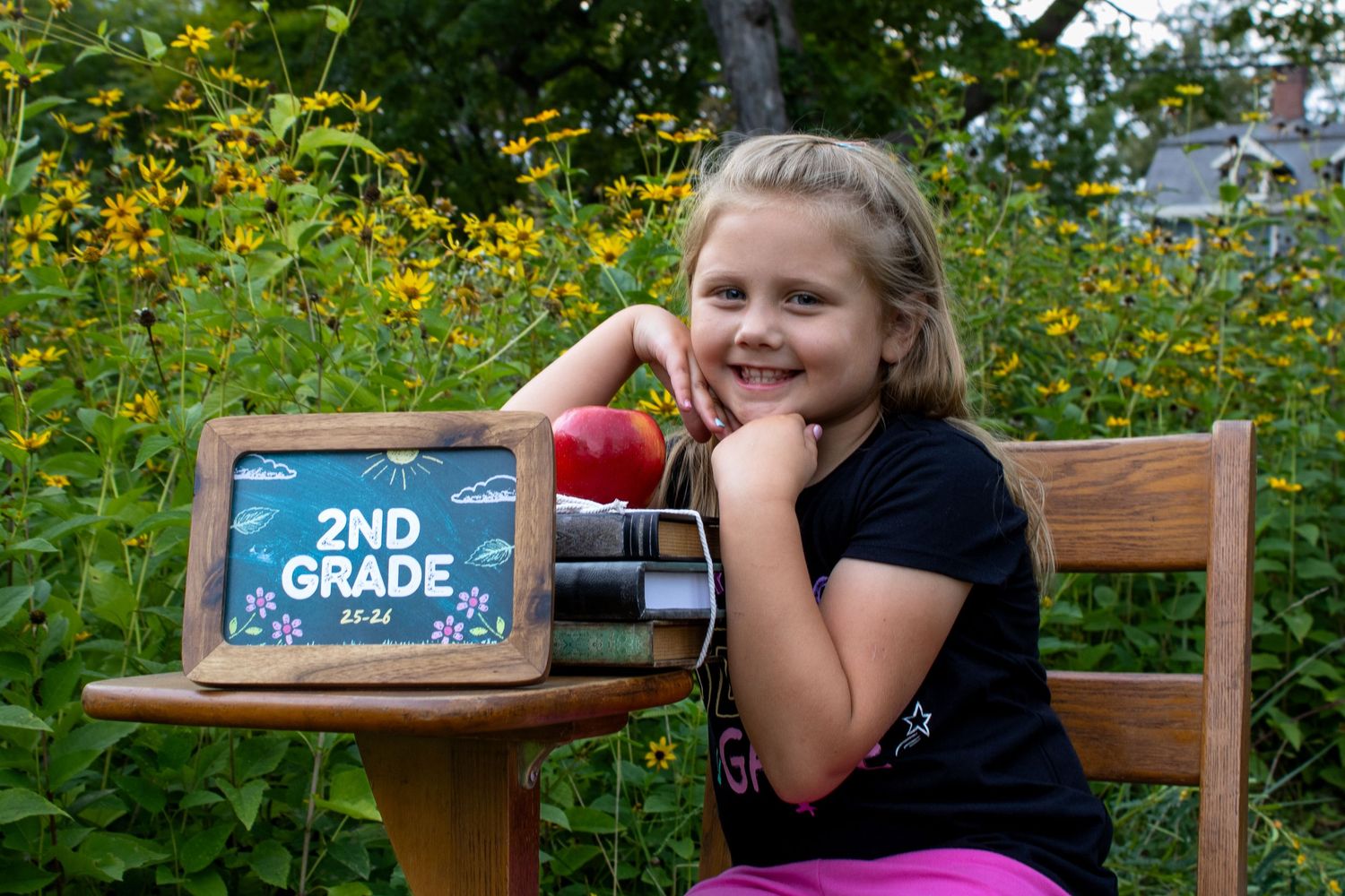 A back-to-school portrait with a chalkboard sign and apple against a garden of yellow flowers.