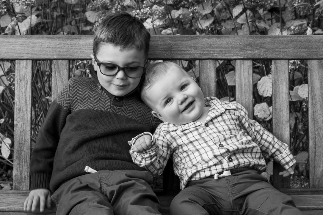 Two children sitting together on a wooden bench in black and white photography.