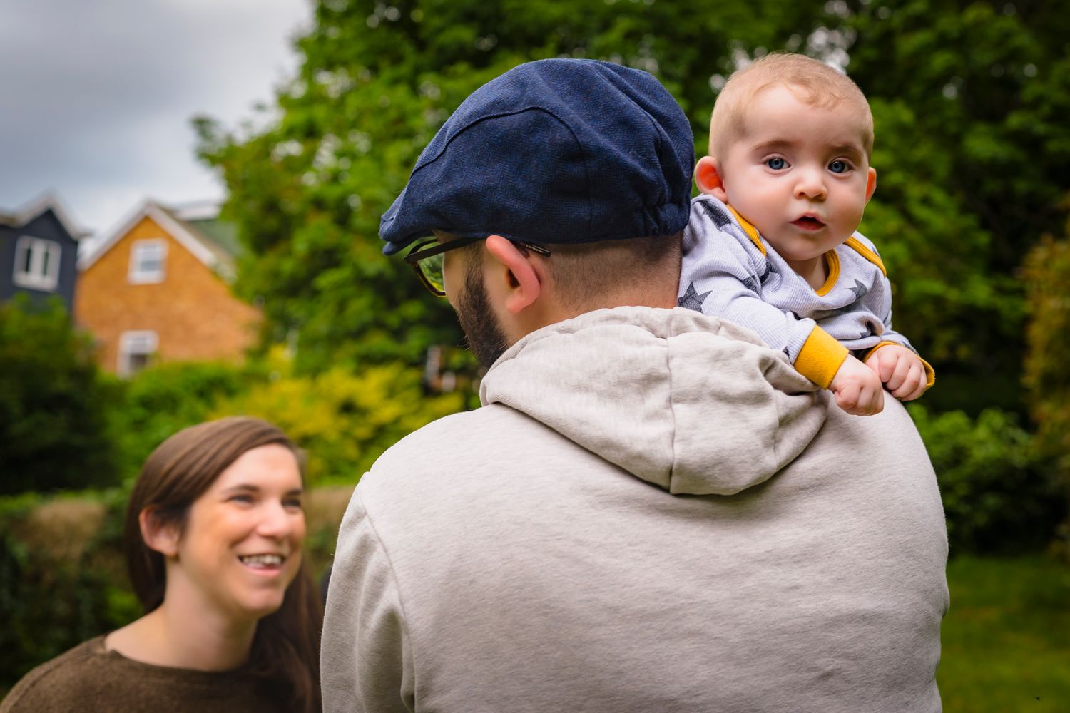 A family of 3 at a Kent park, baby is looking at the camera over her fathers shoulder and the mother is smiling at her partner.
