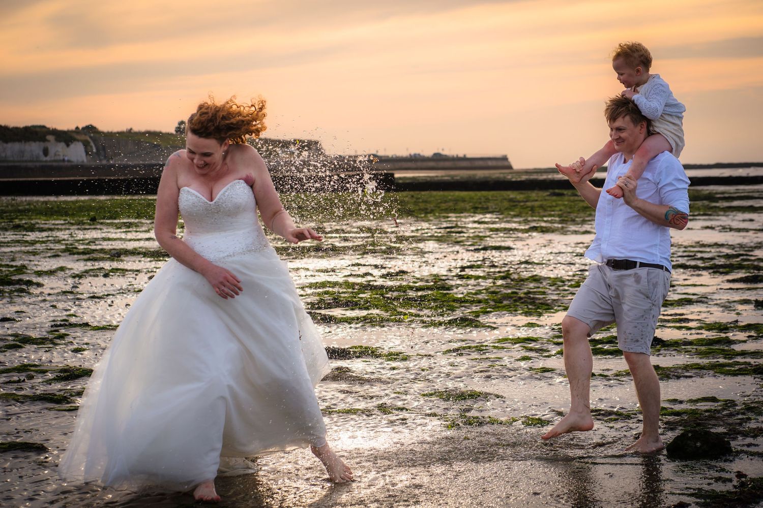 A family on Wesbrook beach at a wreck the dress session, man is smashing sea water at his wife and they are laughing, with Shorely a memory