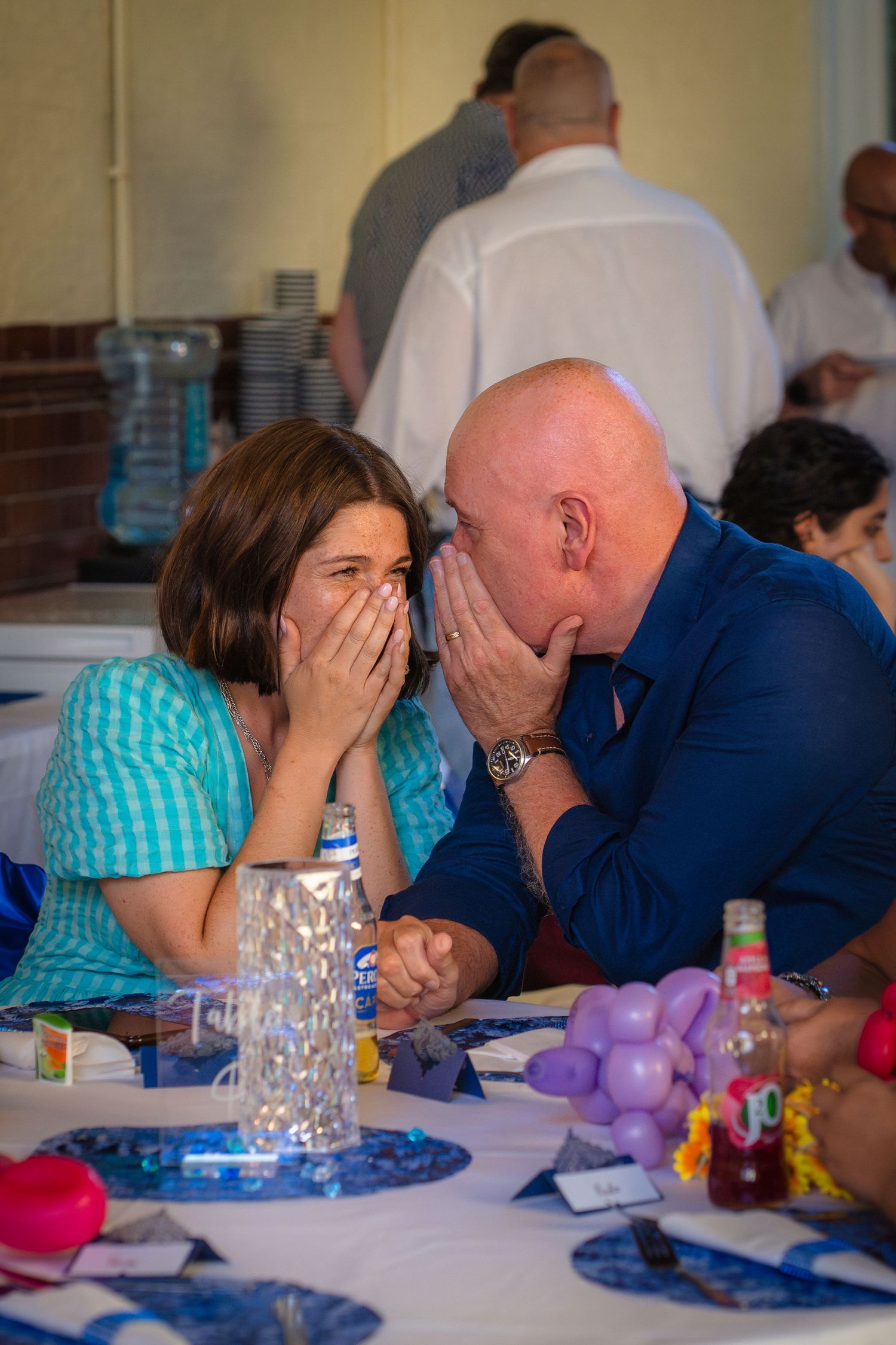 A couple whispering and sharing a joke at a celebration party, candid and unposed capture by shorely a memory.