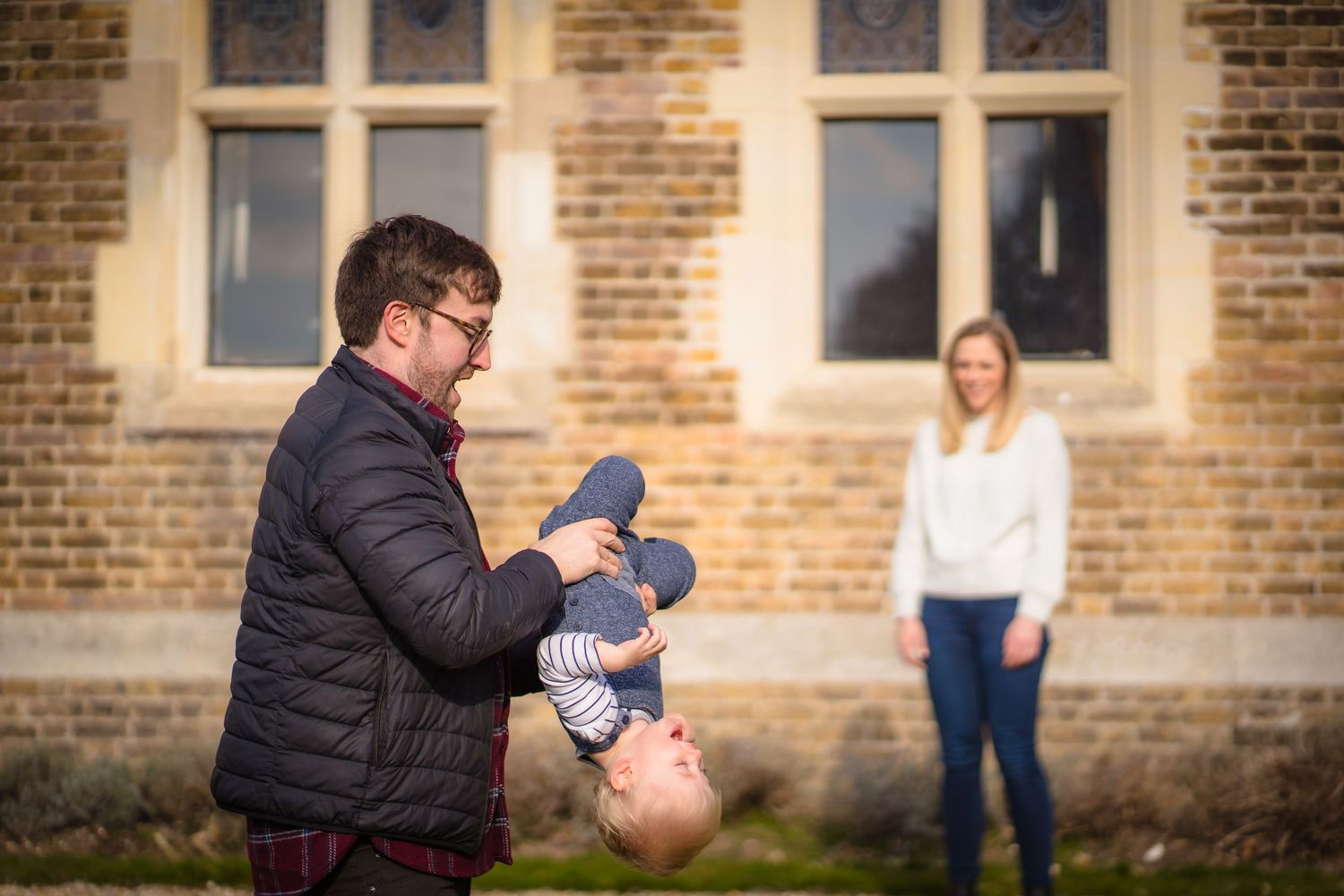 A father playing with his son whilst the mother looks on with a smile. Candid and happy.