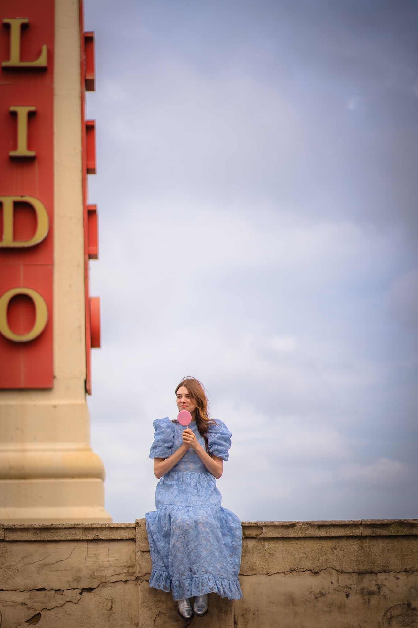 Girl sitting by the Lido in a blue dress and with a lollipop. Cloudy blue skies that compliment her dress. Shorely a memory photography.