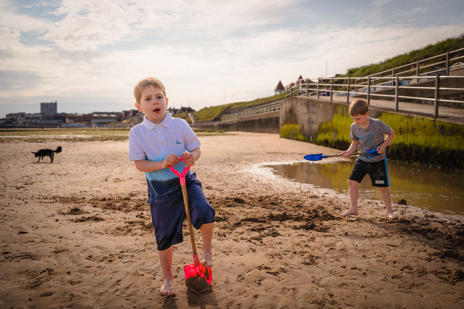 Two boys digging on the beach with the view of Margate behind them.