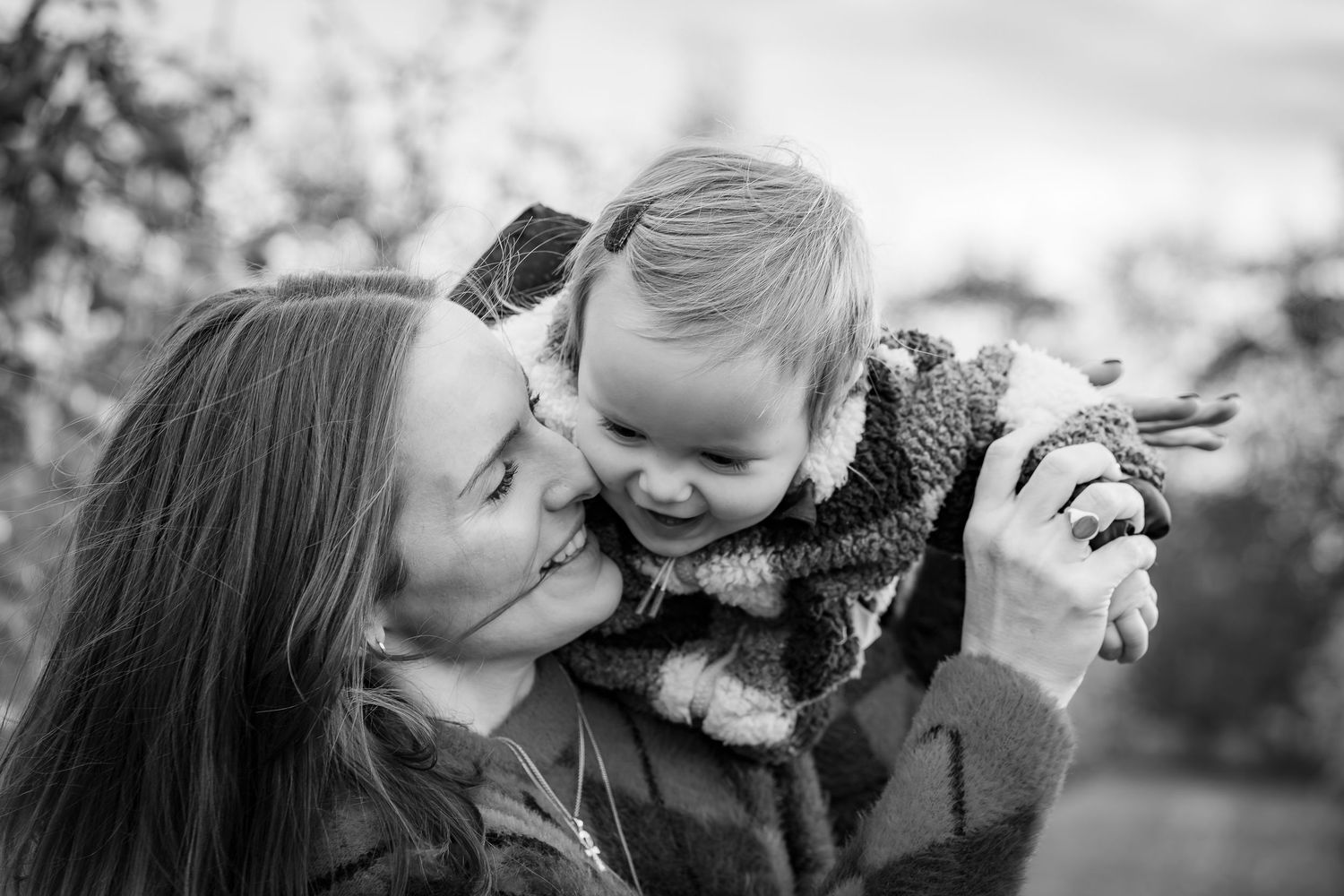 A mother and daughter in an autumnal apple orchard smiling and laughing together, in black and white.
