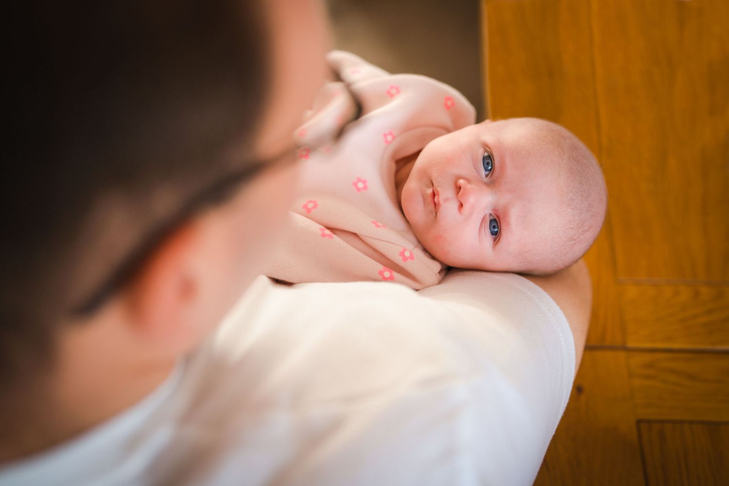 Newborn laying in Dad's arms looking up directly into the camera, in home photo session with Shorely a memory photography in Kent.