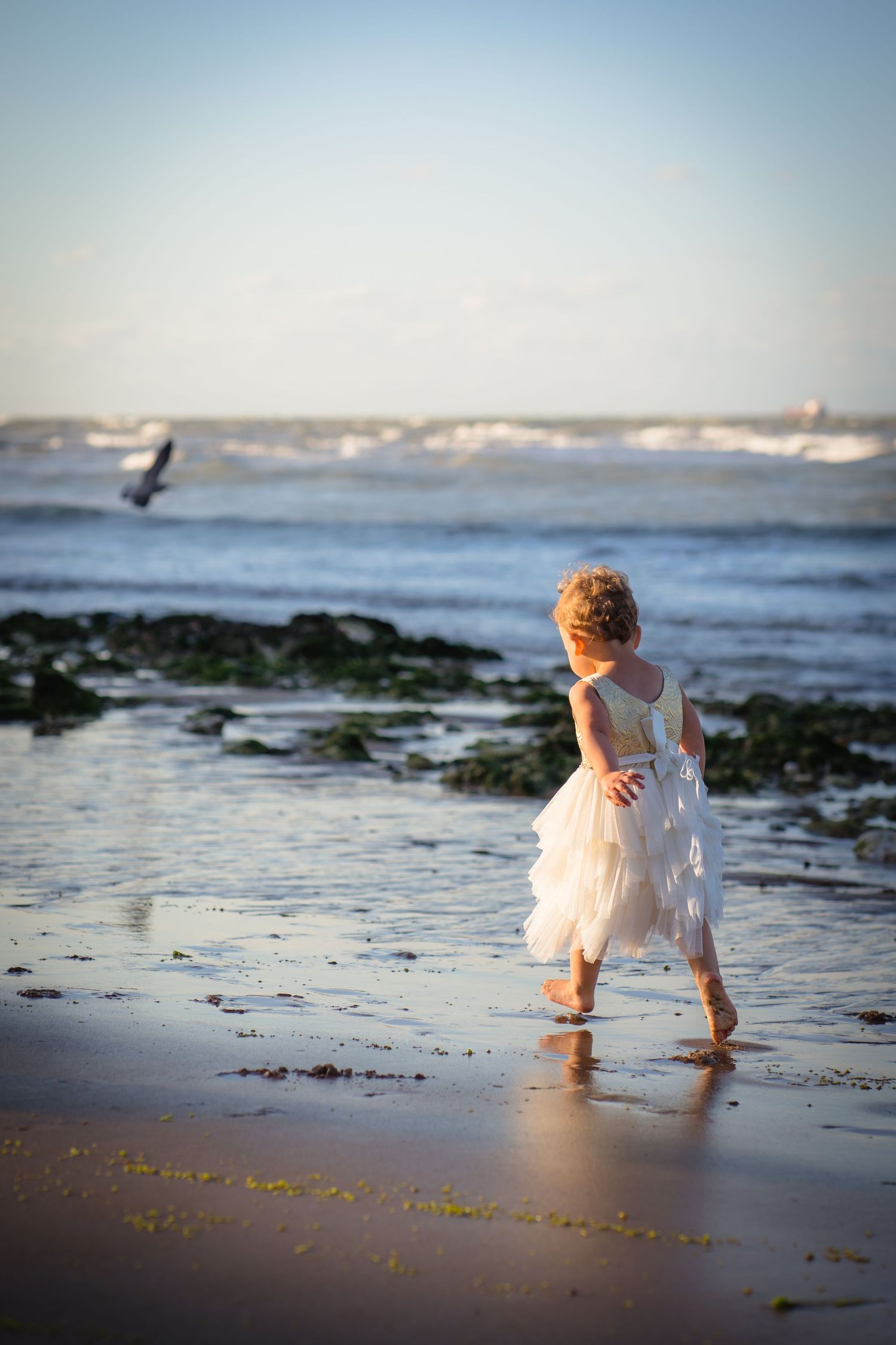A girl in a white dress running along the beach with beautiful light and footprints in the sand at a family session with shorely a memory