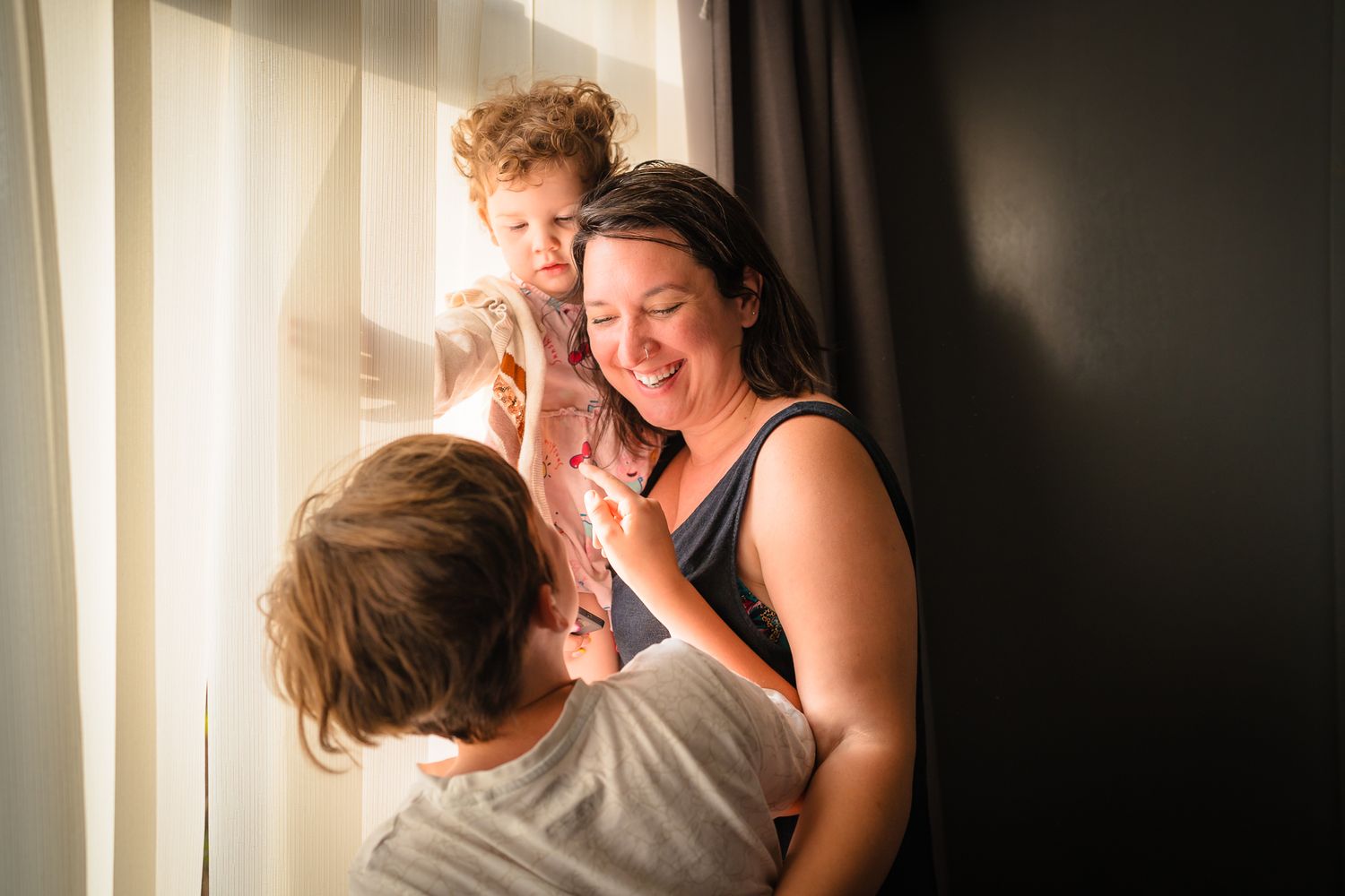 A mother with her two children in front of a window at an in home session. Smiling and loving spending time together.