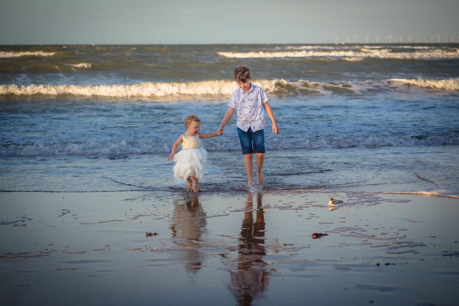 a brother and sister hand in hand whilst walking in the sea at a family photo session with Shorely a memory in margate.