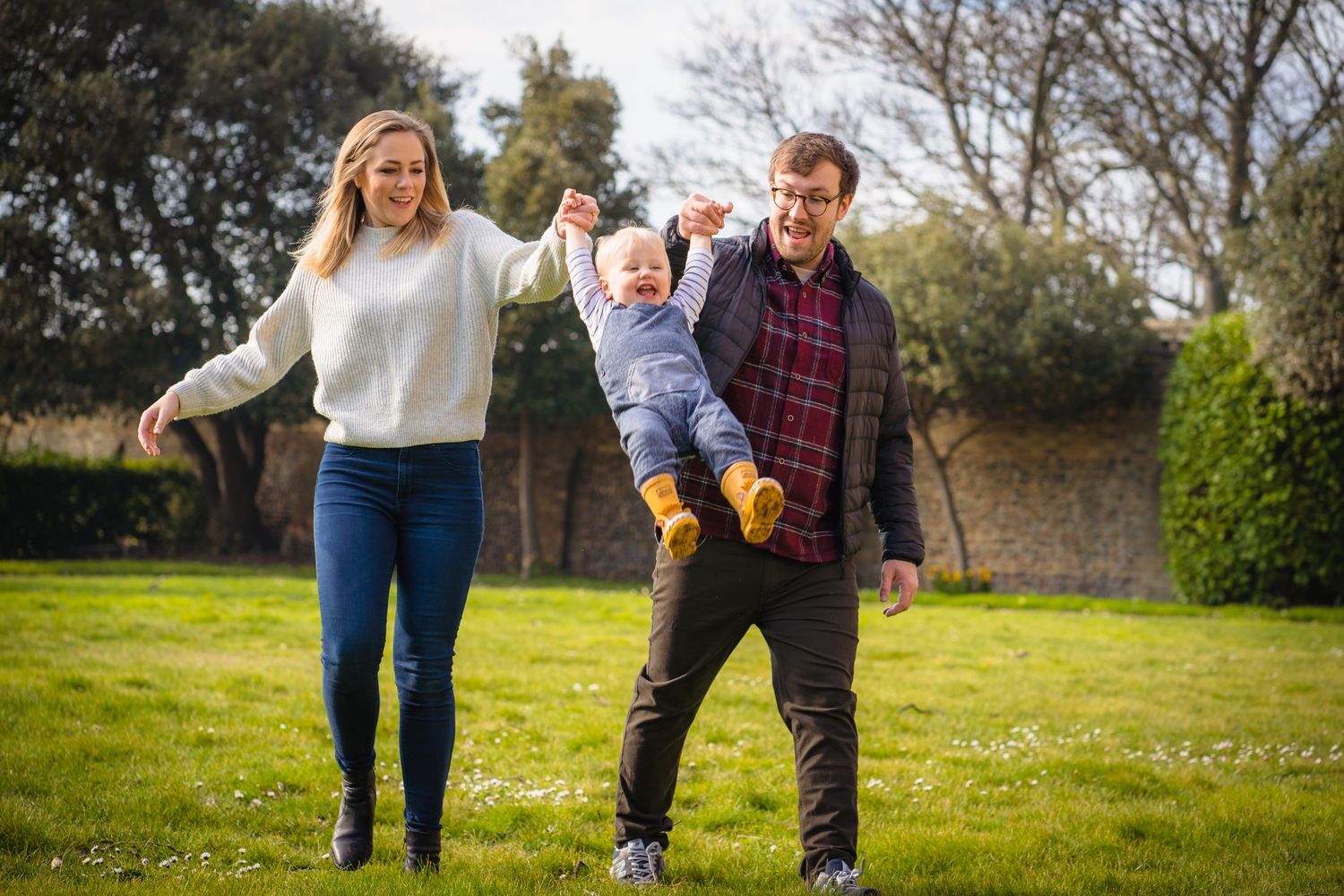 A mother and father swinging their son in the air whilst running through a Kent field on a beautiful summers day