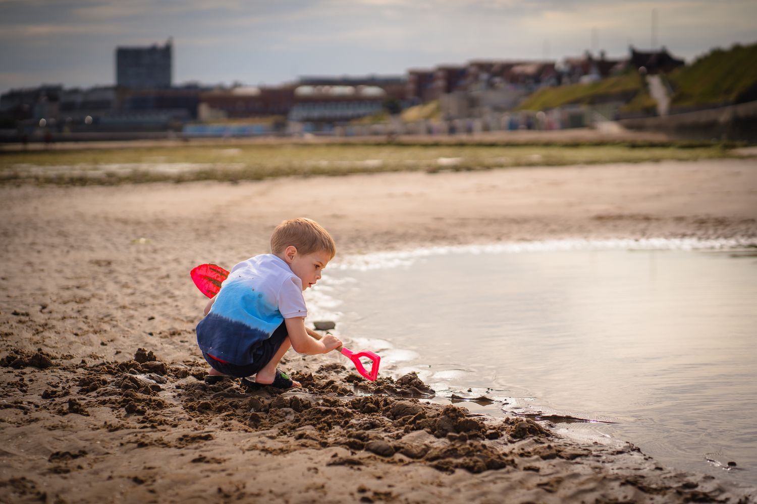 Boy digging on Westbrook beach near the water with the scene of Margate, Kent in the background.