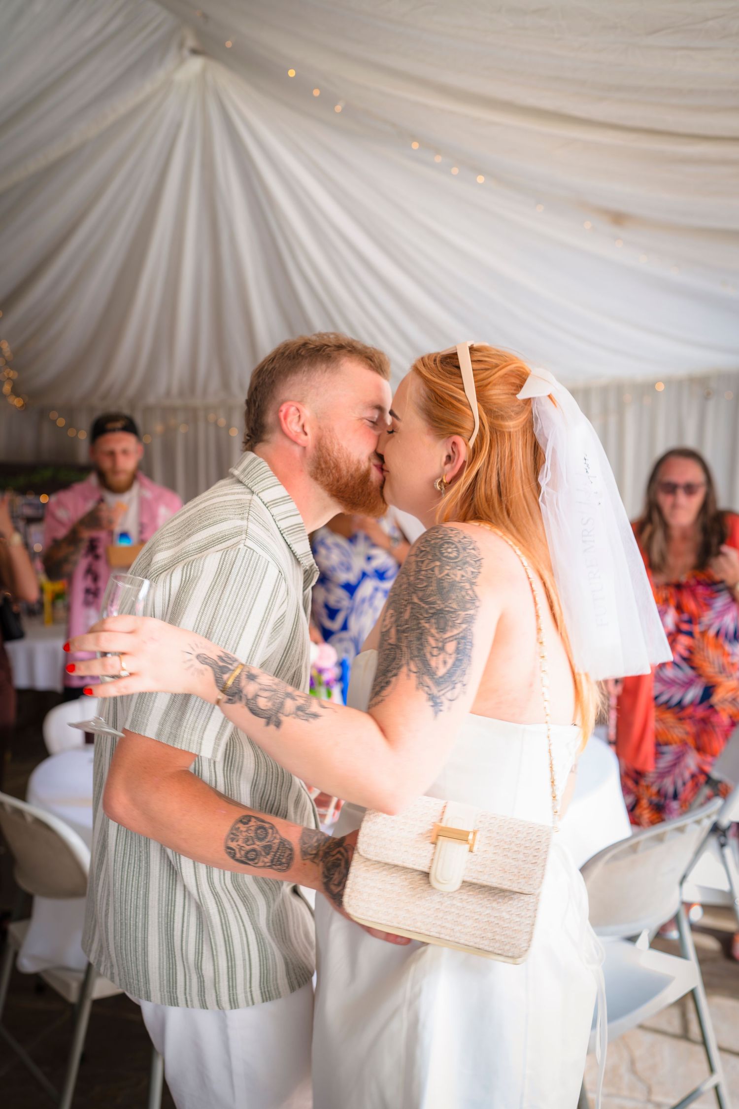 A couple sharing a kiss at an engagement celebration with family and friends.