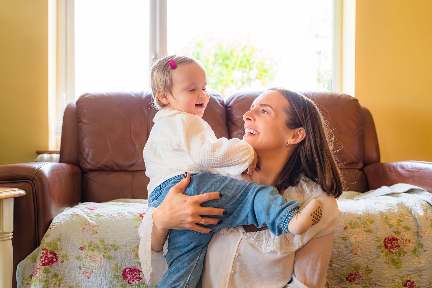 Mother and daughter in home session with yellow walls and beautiful window to back light them smiling and laughing.