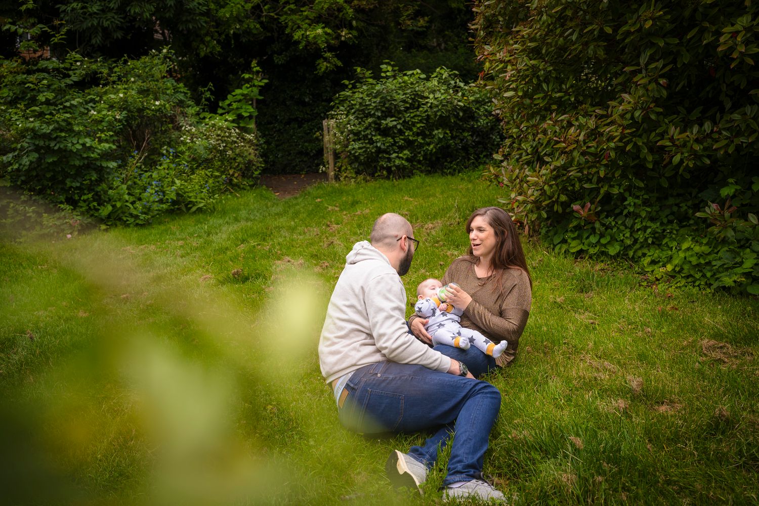 A family of 3 having a quiet moment during a photo session at a Broadstairs park. mother is feeding her baby and looking at her partner