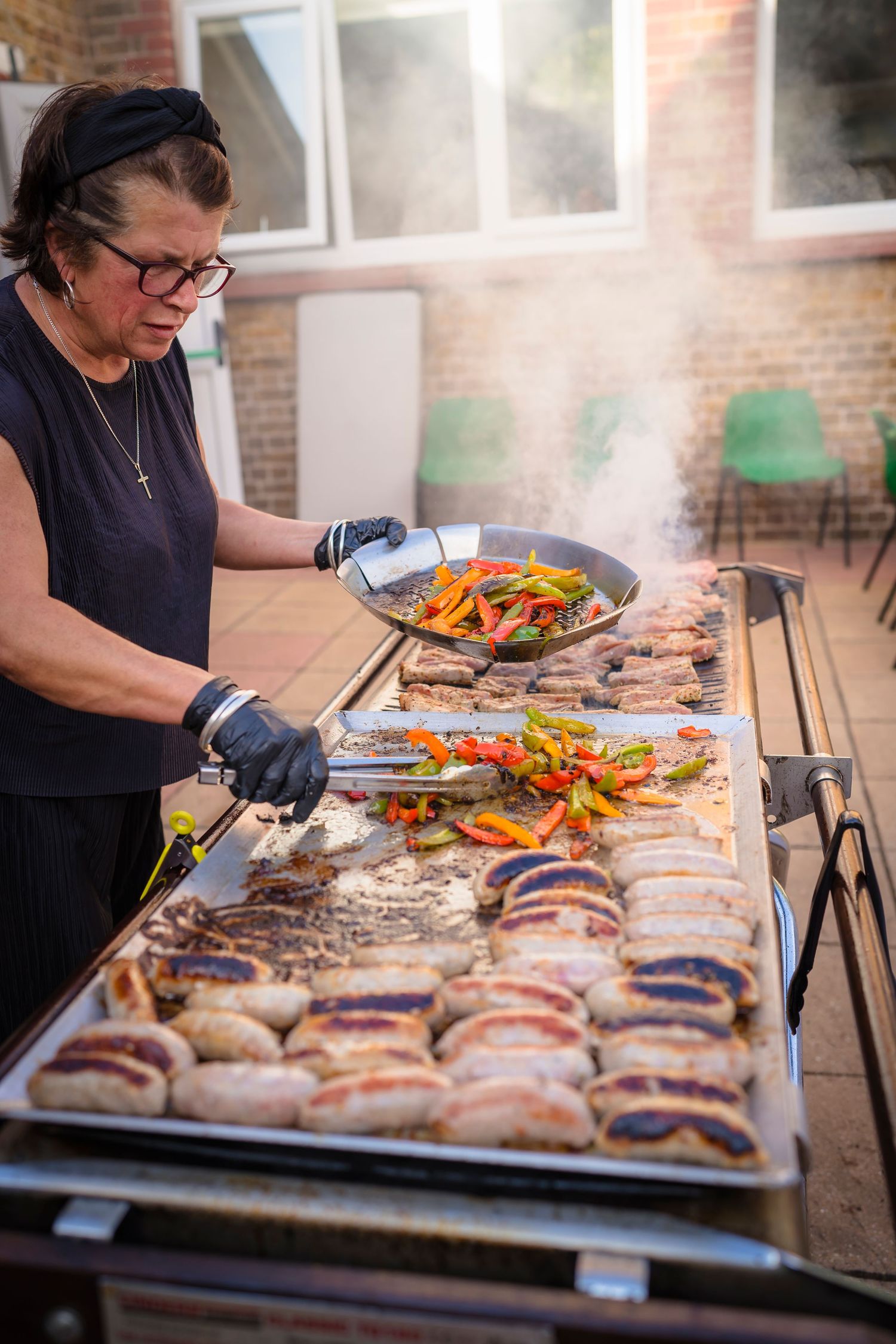 Catering photo of a lady cooking on a BBQ with the delicious food and smoke showing the heat.
