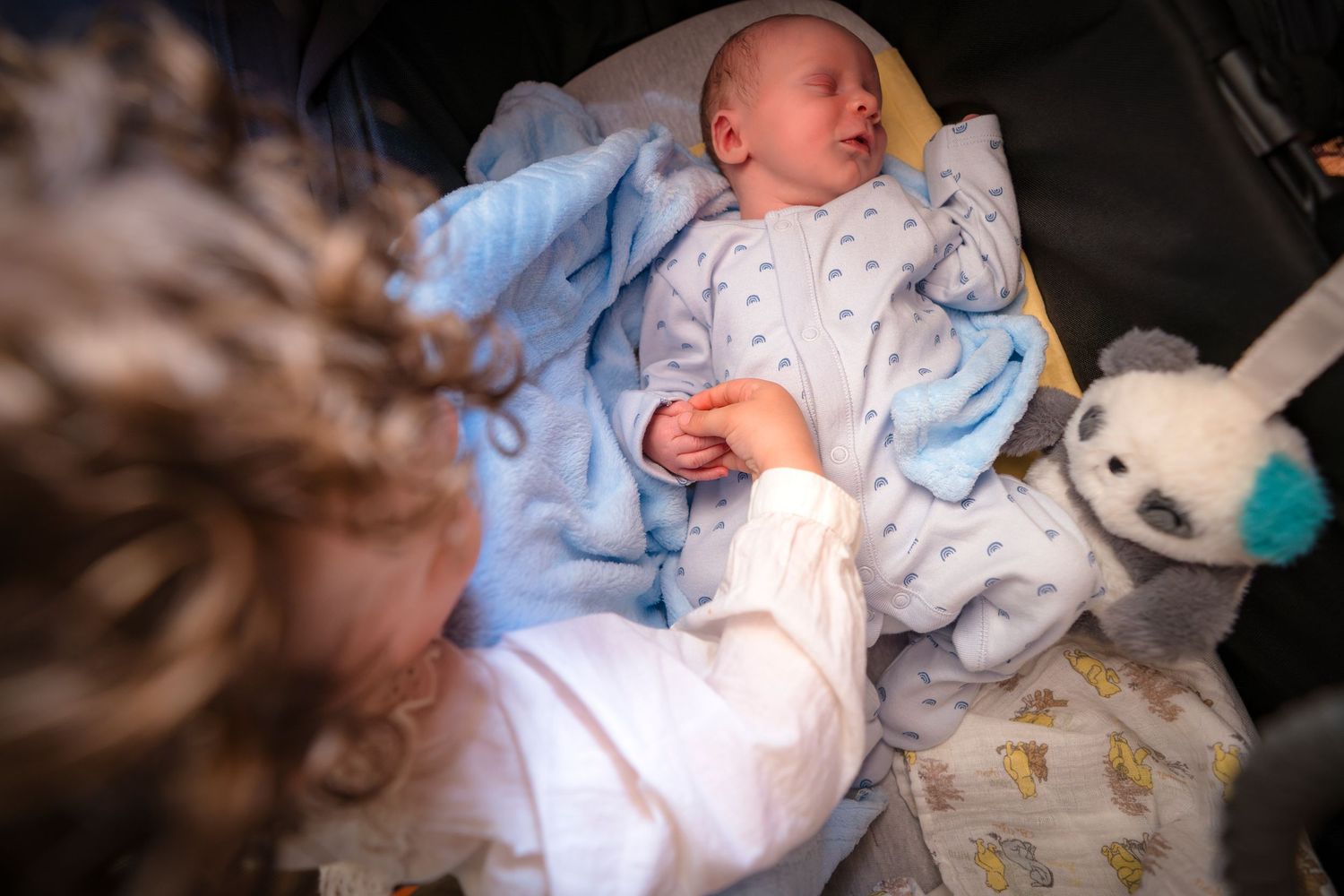 A newborn photo session with older toddler holding the sleeping babies hand at an in home photo session.