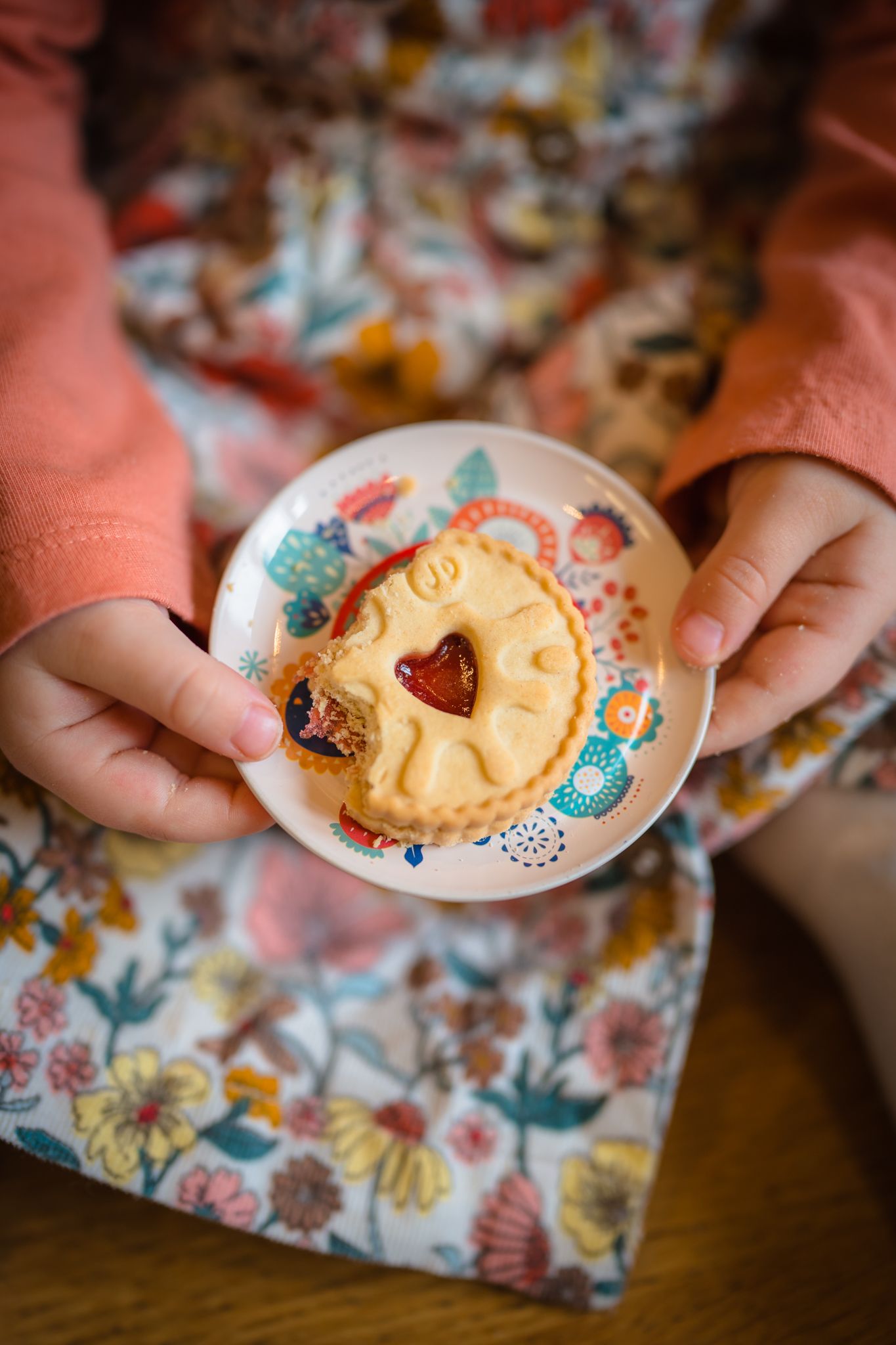 Tiny hands holding a tiny plate with a jammy dodger, vintage style and captured at an in home tea party with shorely a memory photography