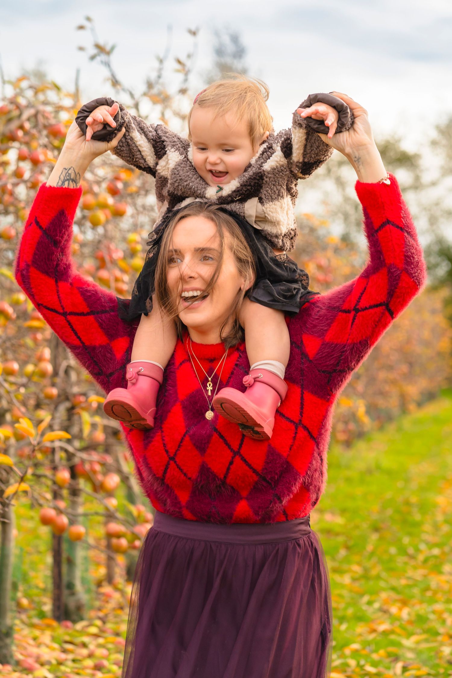 A mother and daughter in an autumnal apple orchard smiling and laughing together.