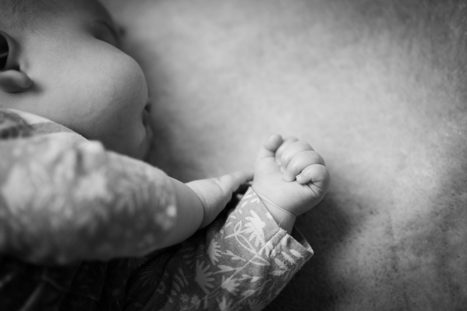 A baby's little sleepy cheek and holding hands in a fist whilst sleeping on a blanket at an in home photo session.
