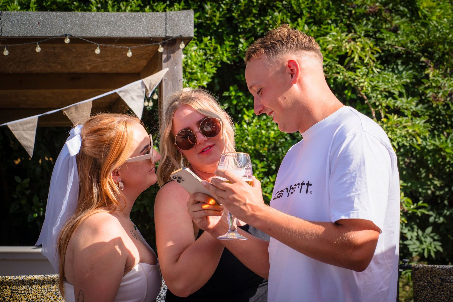 Three friends looking at a phone and sharing a moment together at a family gathering.