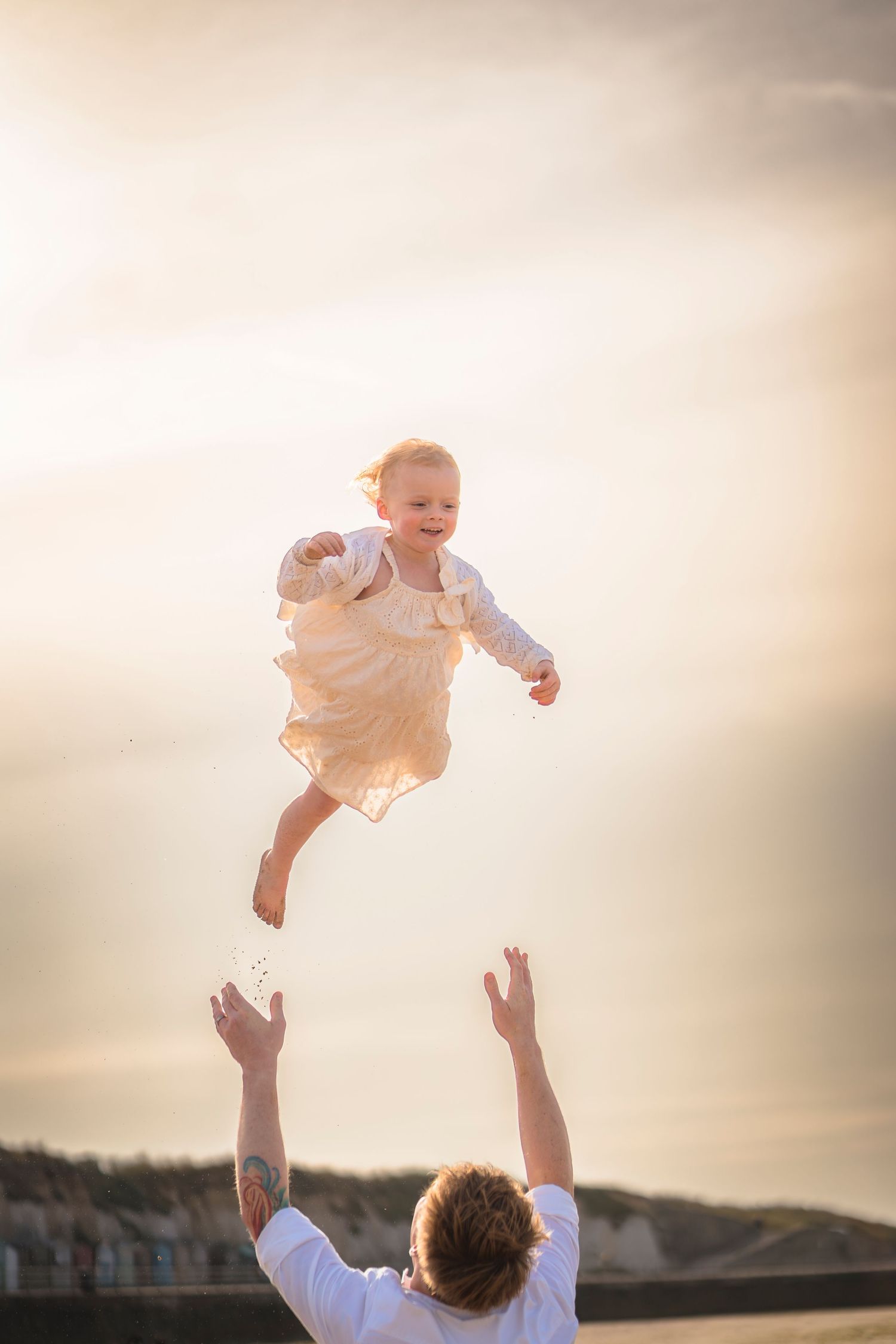 A father throwing his daughter skyward and catching her again, she has a big smile at a beach photo session.