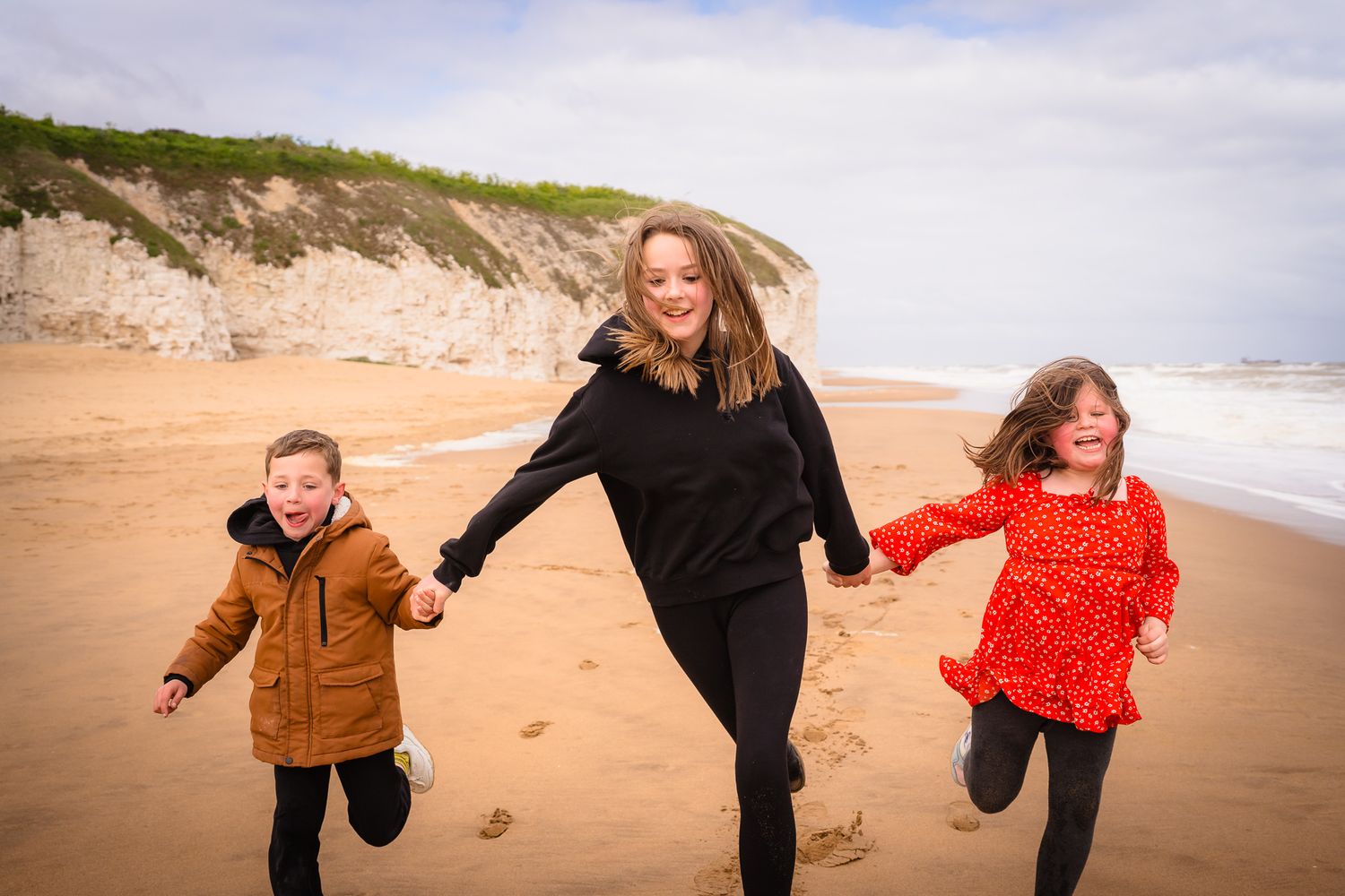 three siblings running towards the camera on Botany Bay Beach, all laughing and holding hands with shorely a memory.