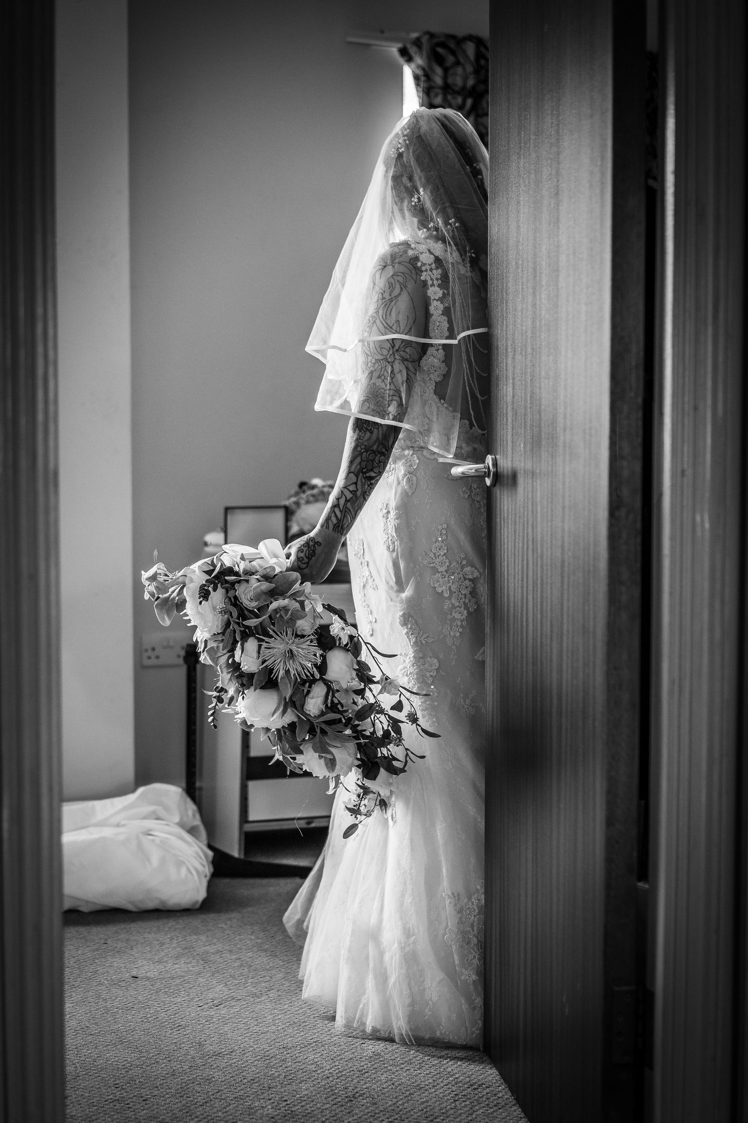 Black and white image of a bride behind, beautiful large bouquet with a window light highlighting the bride.