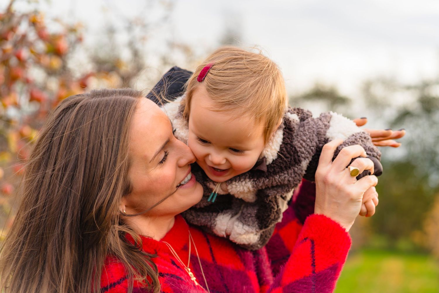 A mother and daughter in an autumnal apple orchard smiling and laughing together.