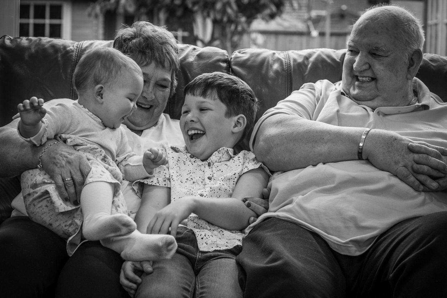 Grandparents with their grandchildren, cuddling and laughing  on a sofa in black and white.