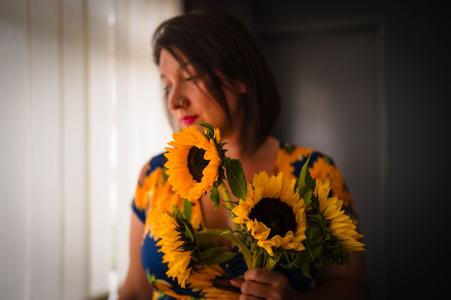 Portrait of a woman standing in front of a window holding a bunch of sunflowers, in home photo session.