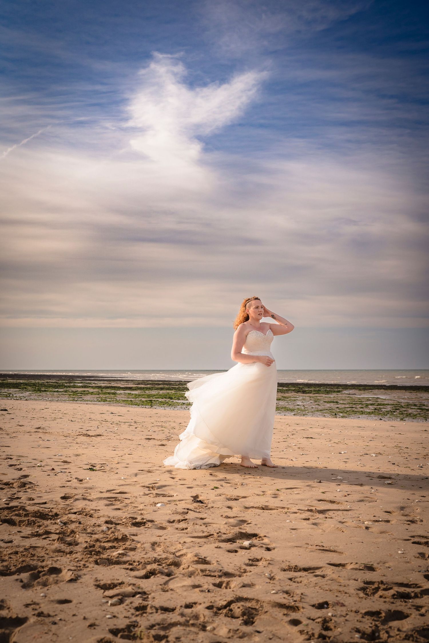 Powerful image of a lady in a gown on the beach, wind in her hair and blowing the dress, sea and clouds behind her and beautiful light