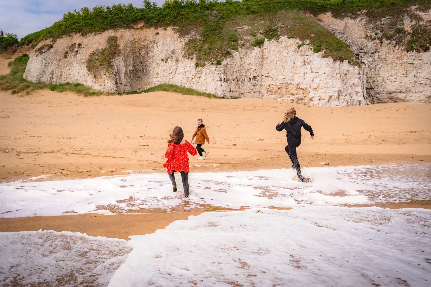 three siblings running from the sea at a Kent beach, candid, unposed fun during a family session with shorely a memory photography