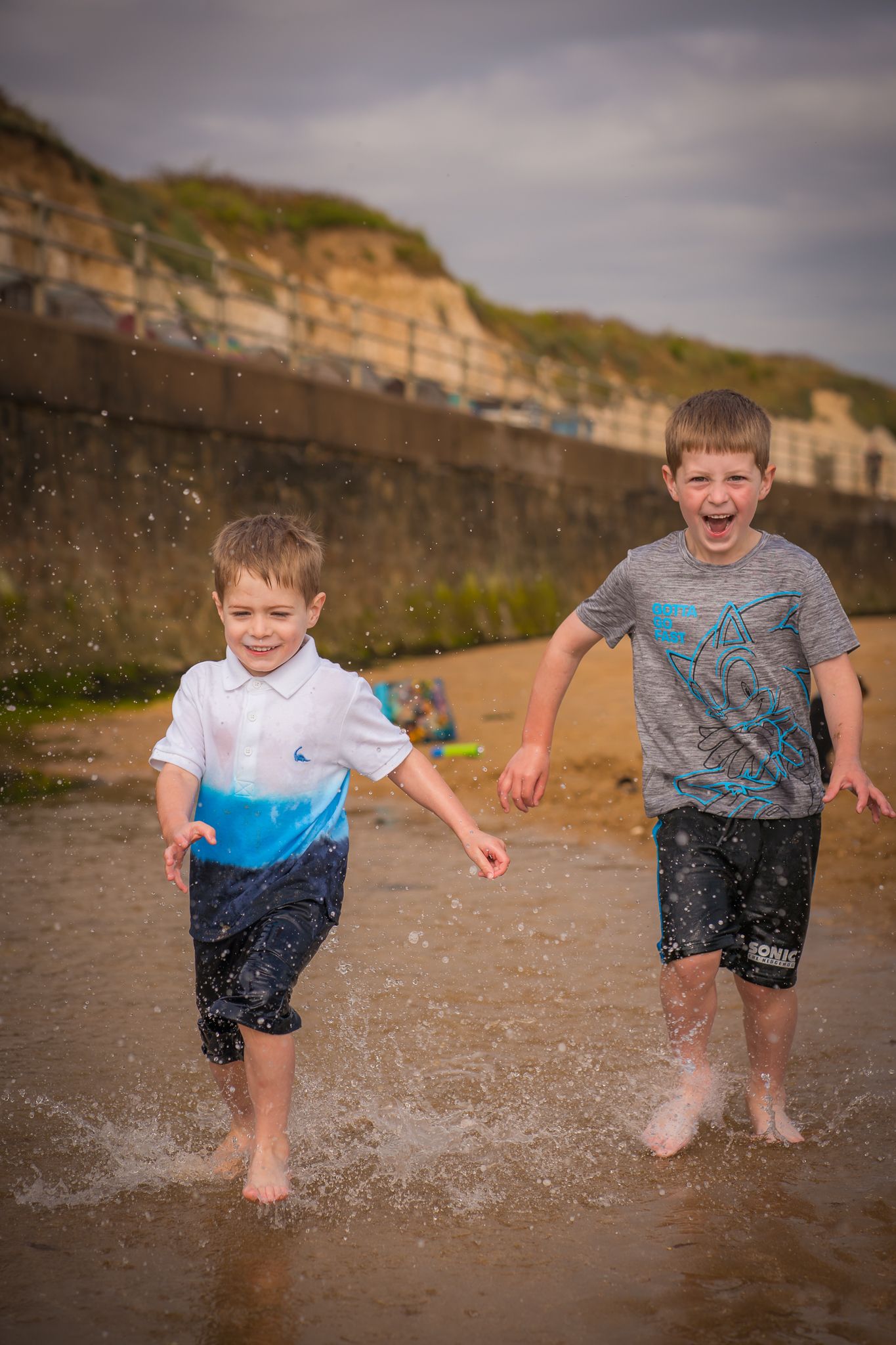 Two boys running towards the photographer laughing and splashing in the water on Westbrook beach in Margate, Kent.