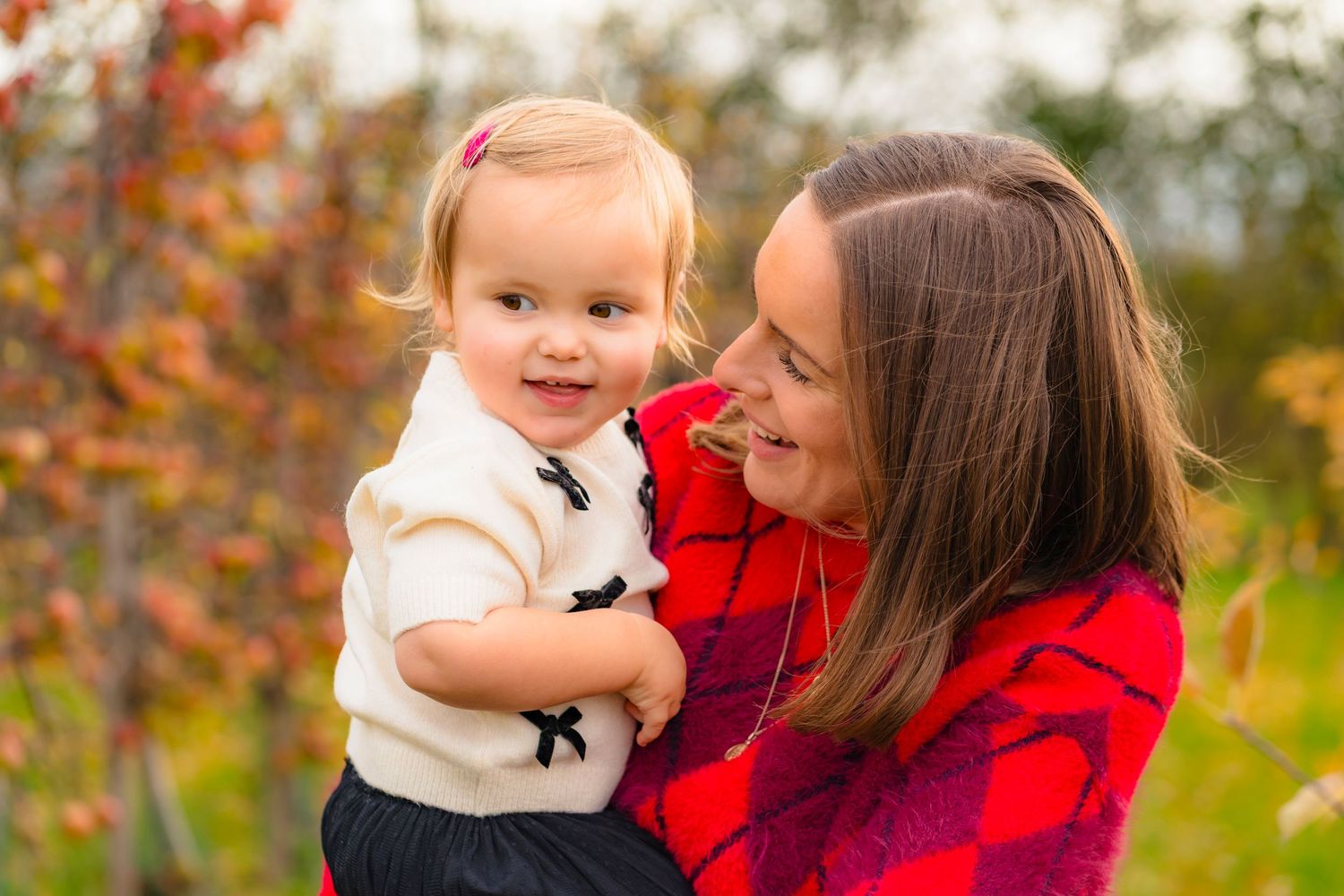 A mother and daughter in an autumnal apple orchard smiling and laughing together.