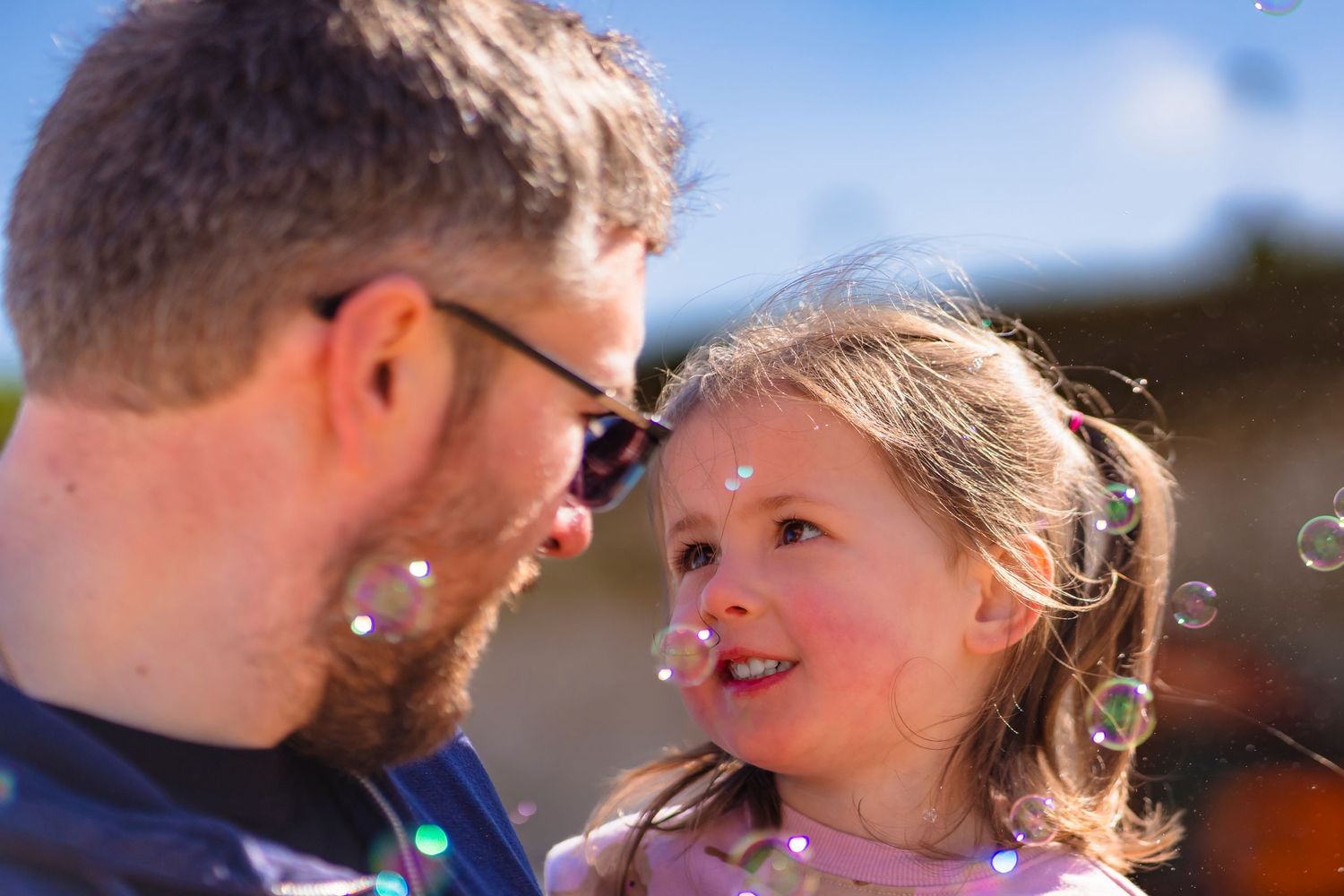 A colour image of a father and daughter looking into each other's eyes whilst bubbles are flying around them.