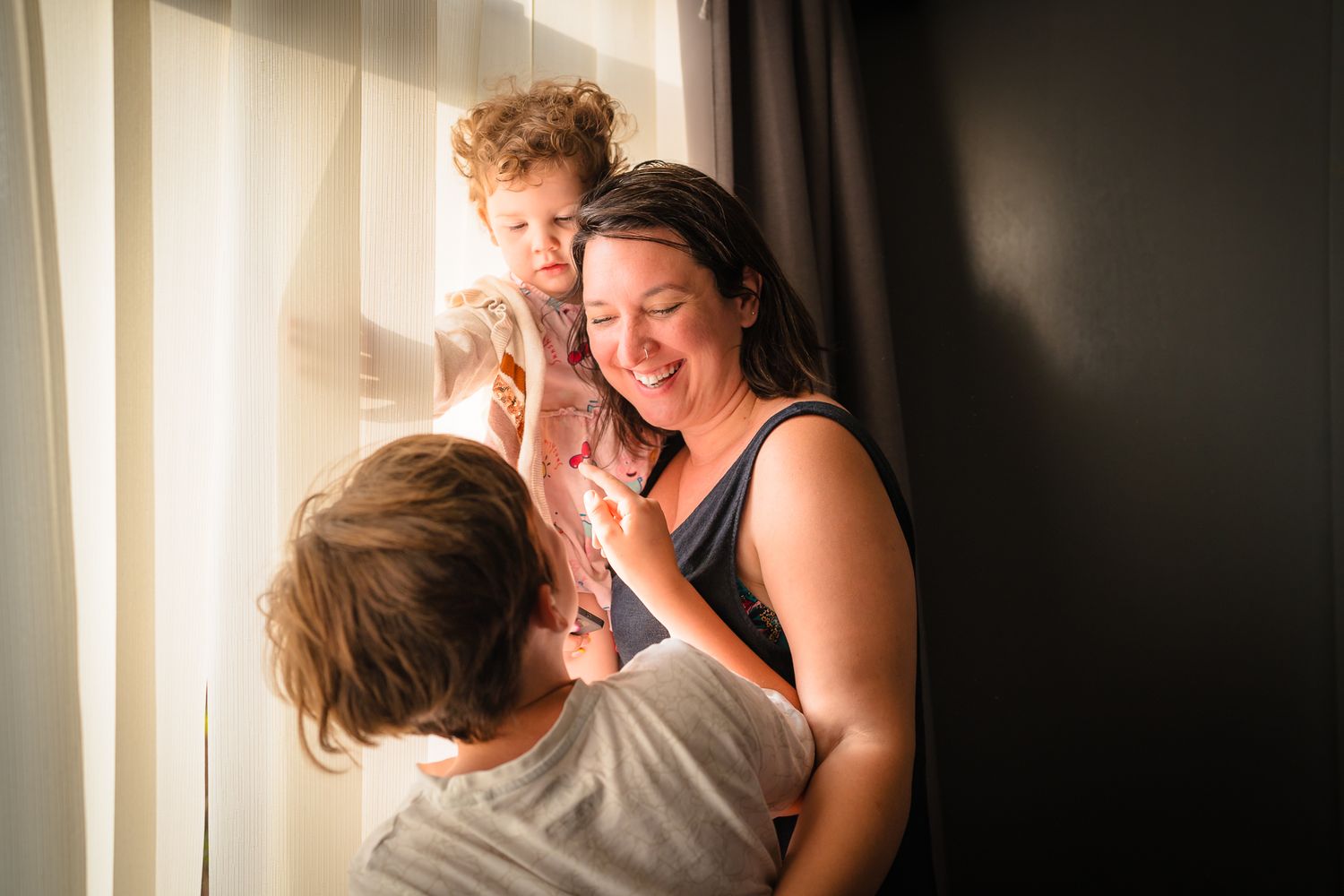 A mother with her two children in front of a window at an in home session. Smiling and loving spending time together.