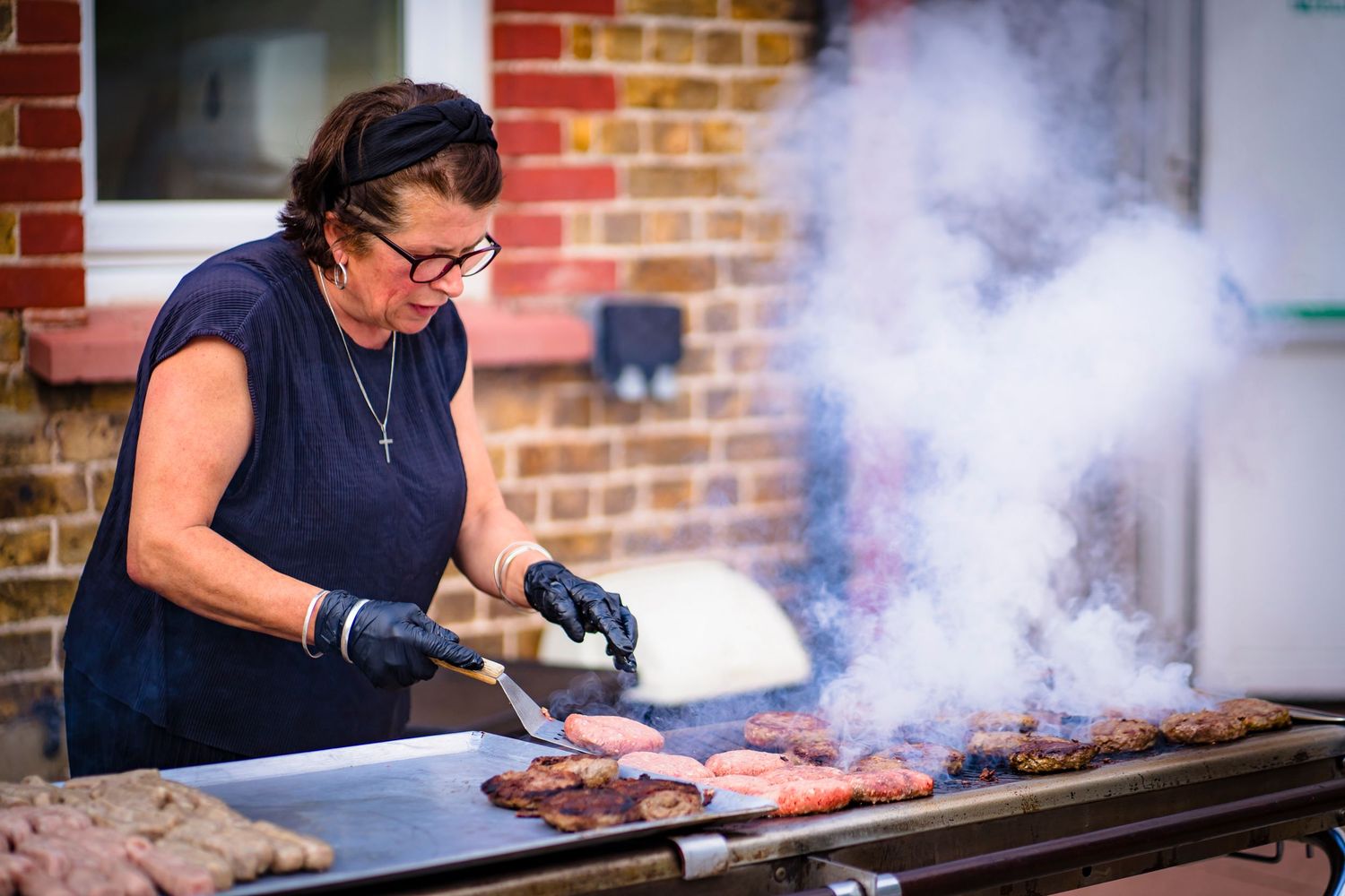 Catering photography of a lady BBQ'ing at a family gathering event. Smoke is highlighted and showing the heat coming from the food.