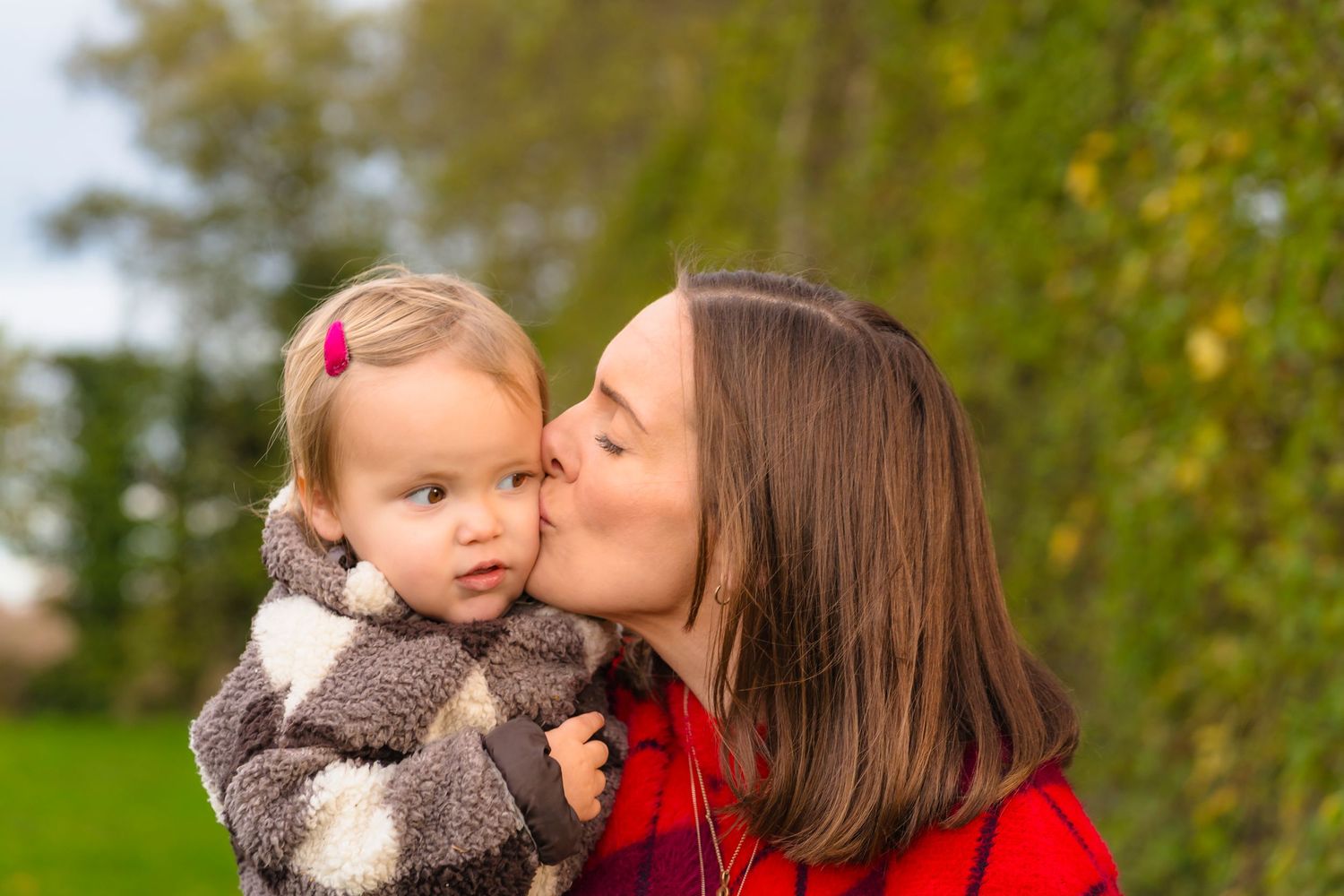 A mother and daughter in an autumnal apple orchard smiling and laughing together.