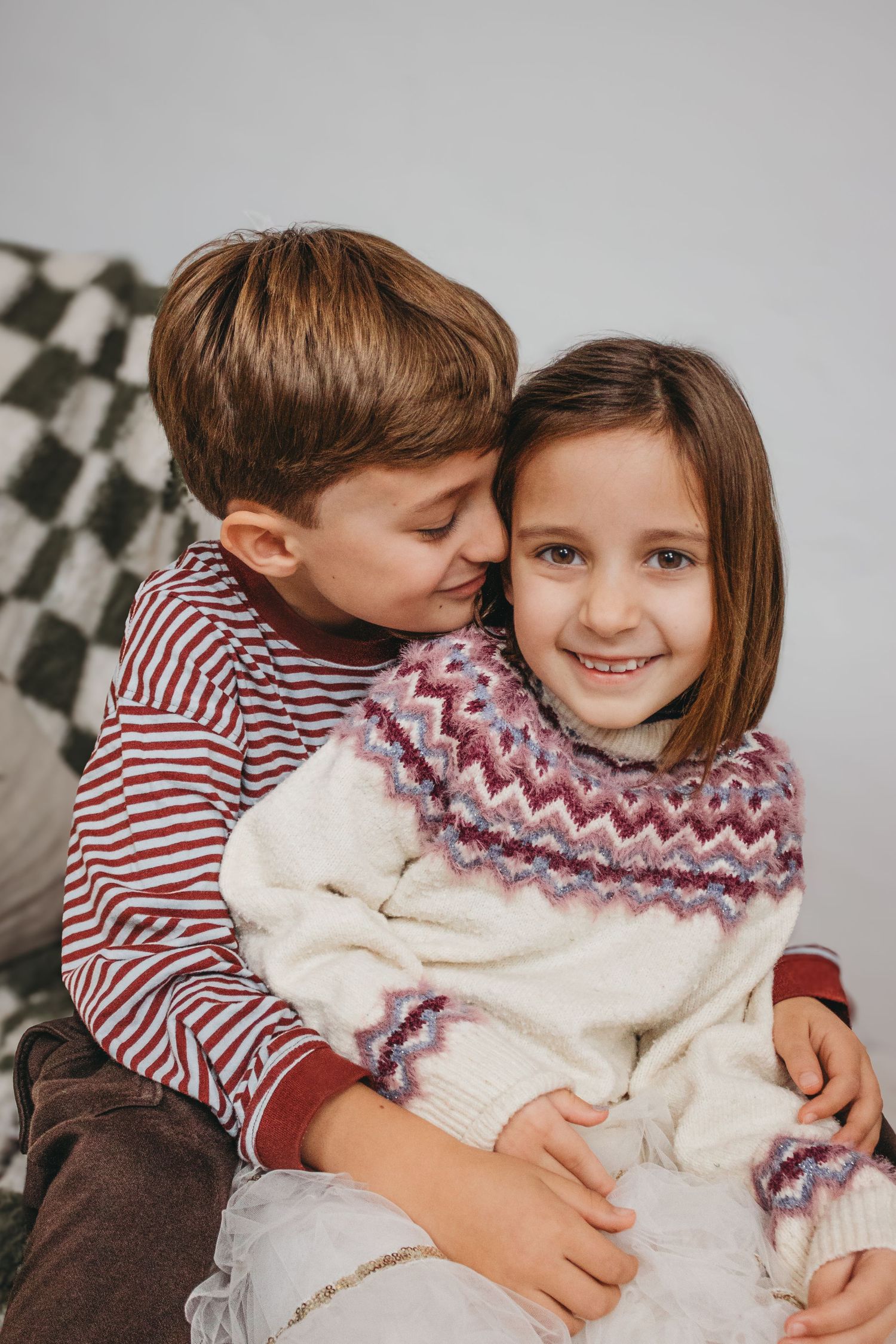 Two children share a sweet moment wearing cozy winter attire in red and white stripes and knit scarves.