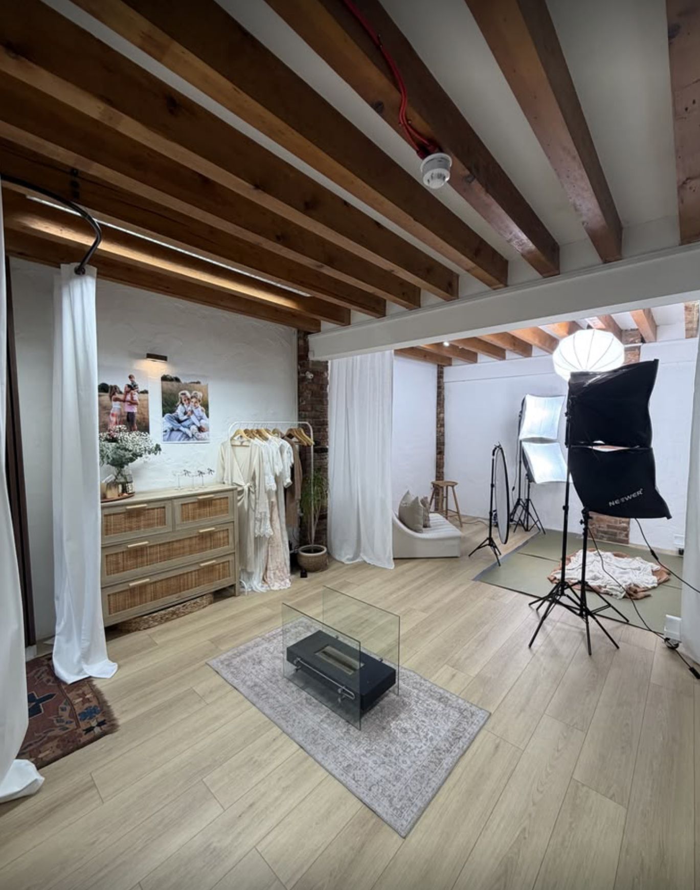 A panoramic view of a photography studio with wooden beams, lighting equipment, and white backdrop setup.