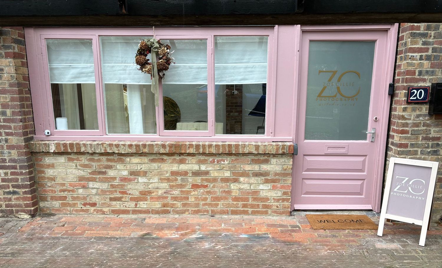 A charming storefront with pink door, exposed brick wall and 'ZC' signage features large windows with delicate decor.