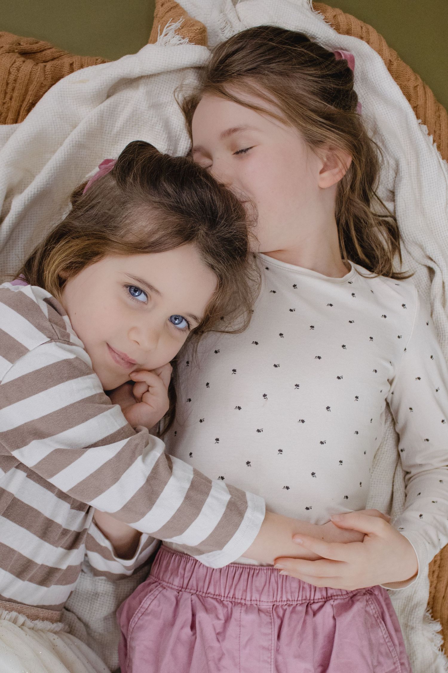 A series of sweet close-up shots showing two children cuddling together in polka dot and striped outfits on a bed.