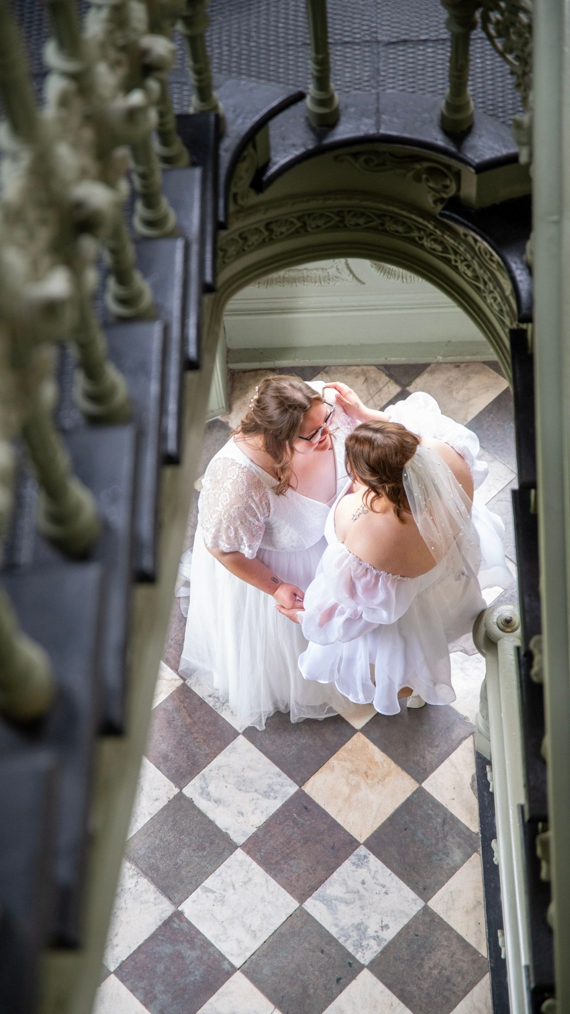 Birds-eye view of two people in flowing white gowns on diamond patterned flooring.