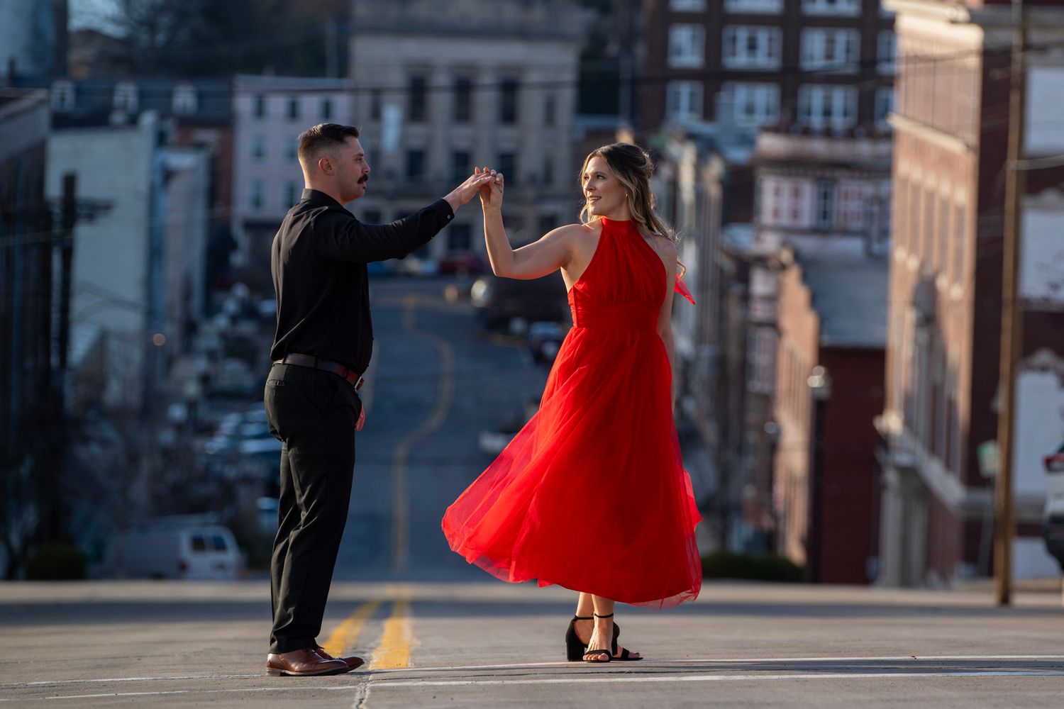 Figures dancing in an urban setting with one wearing a vibrant red dress.