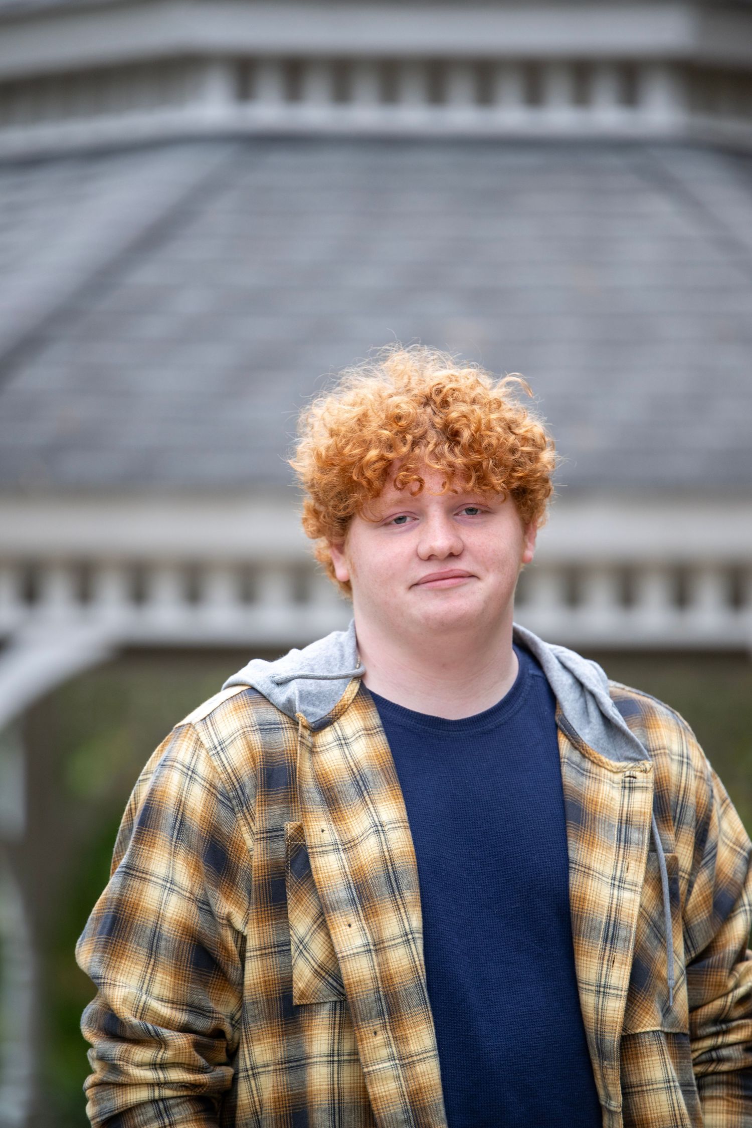 Portrait of person in plaid jacket and navy shirt standing in front of architectural structure.