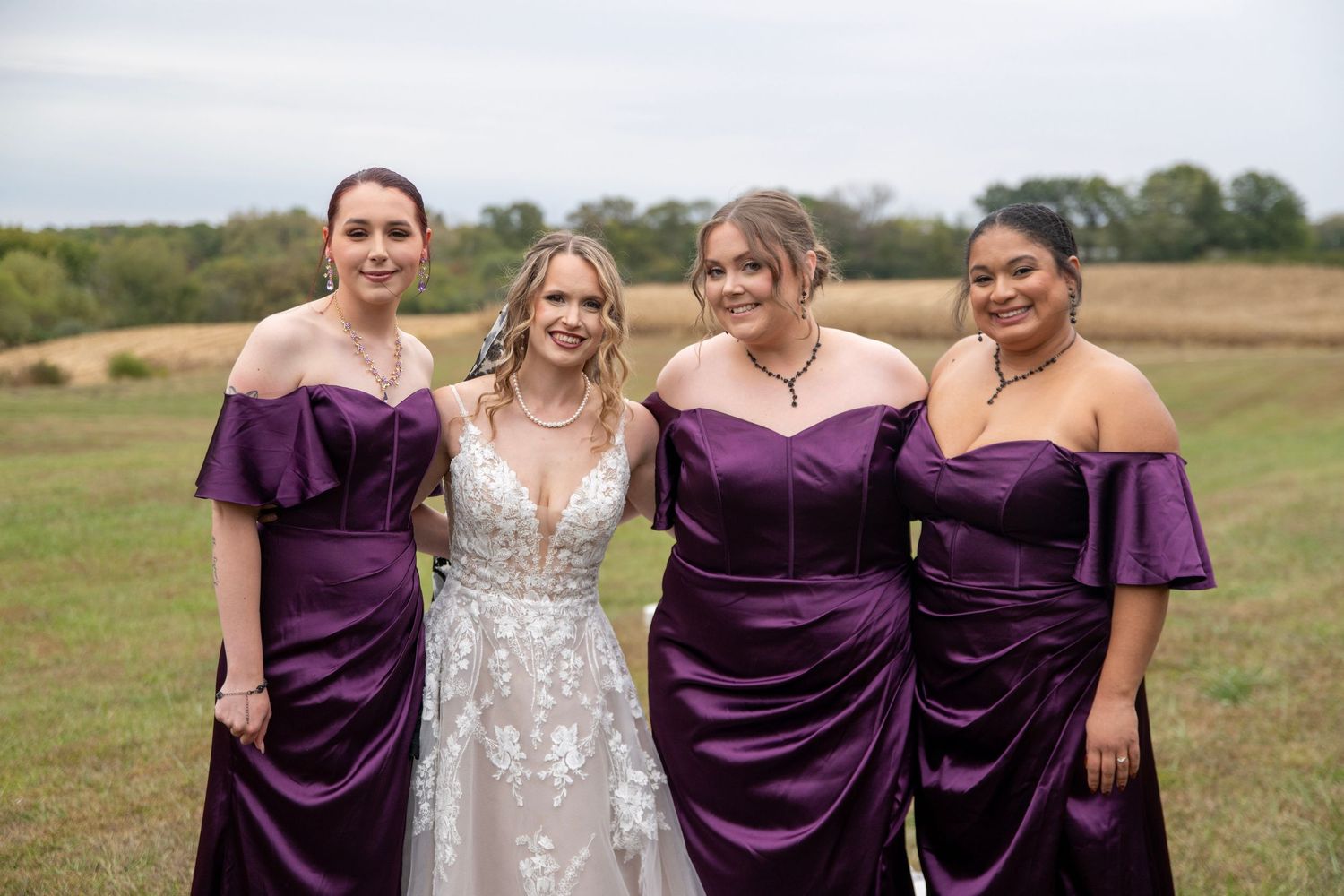Wedding party in purple dresses posing outdoors at lakeside venue.