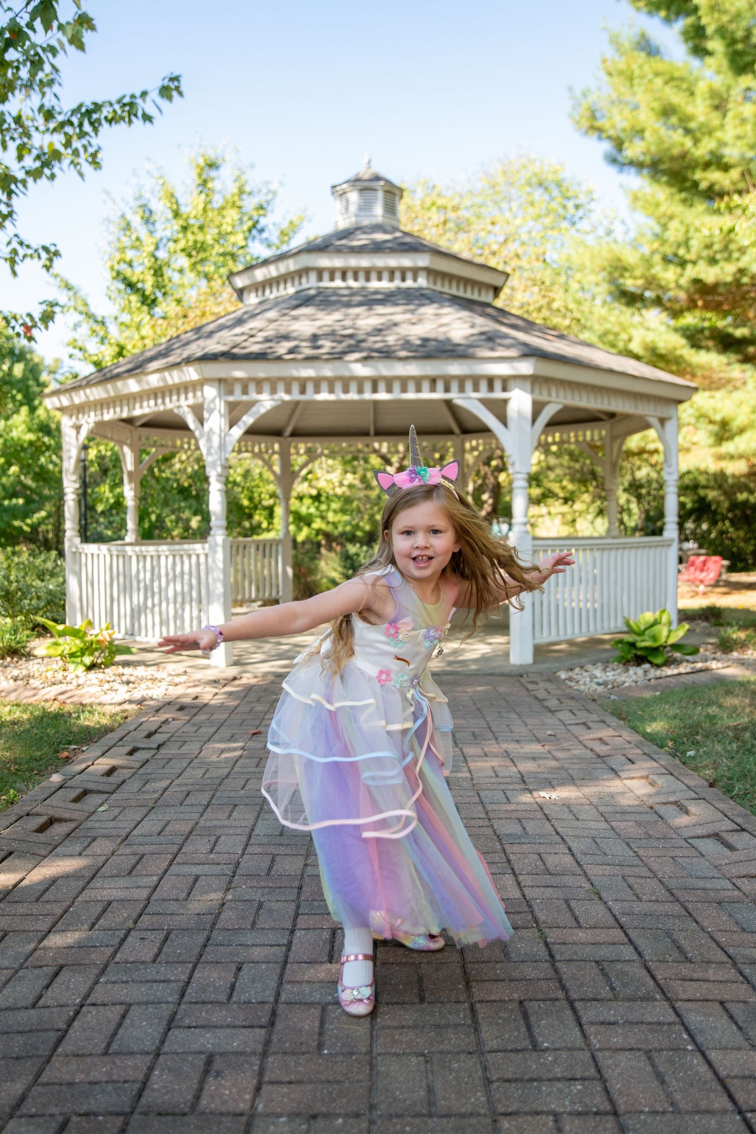 Energetic sequence of a child dancing and spinning in a fairy dress near a white gazebo.