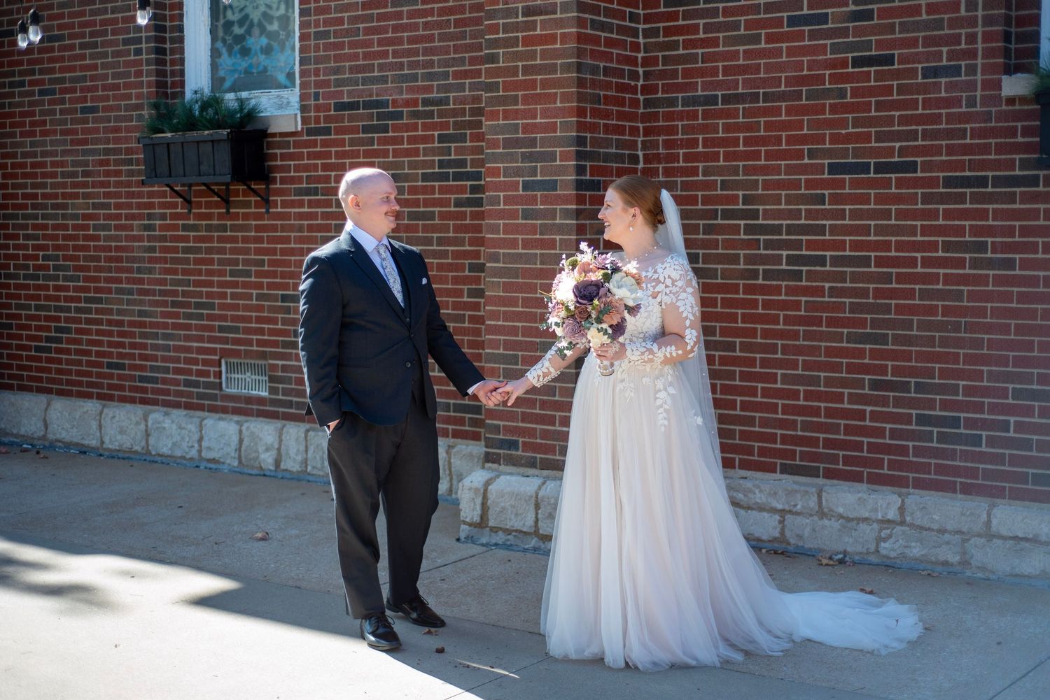 Wedding couple and party take formal photos outside brick building.