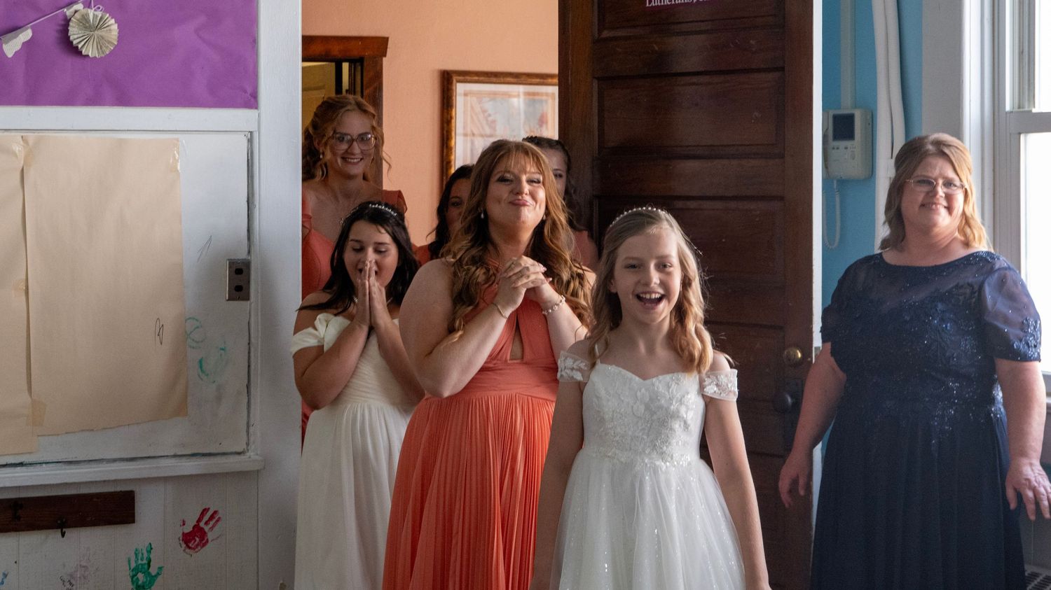 Wedding party members in coral and navy dresses gathered in an indoor setting.