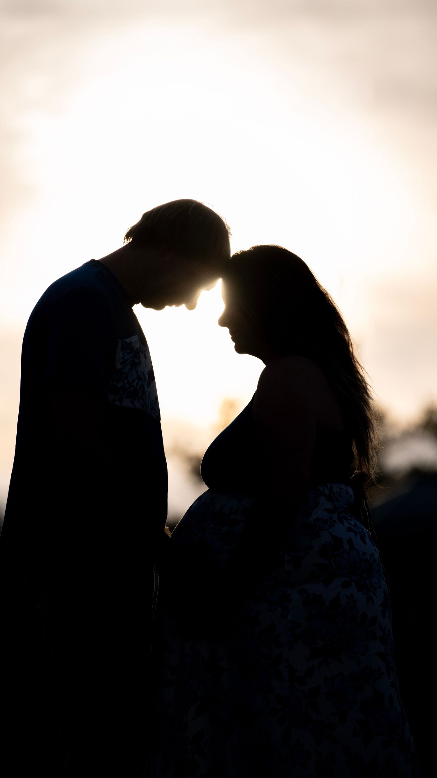 Silhouetted couple sharing an intimate moment against a soft sunset sky.